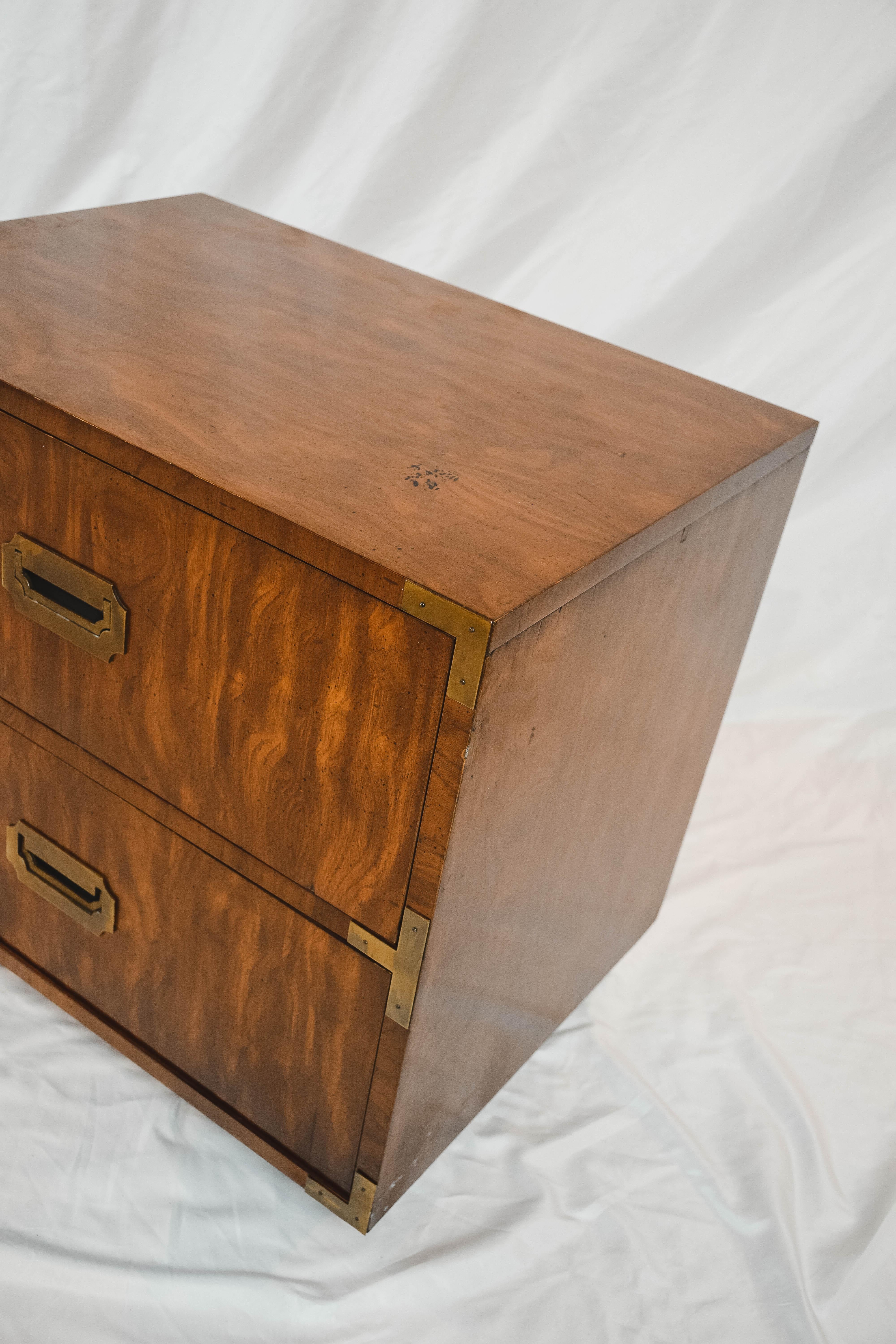 A pair of Campaign style end tables by Dixie Furniture, mid-20th century. This pair of end tables feature a rectangular top and conforming case with two stacked drawers featuring brass hardware. Each piece is hallmarked Dixie Campaigner inside the