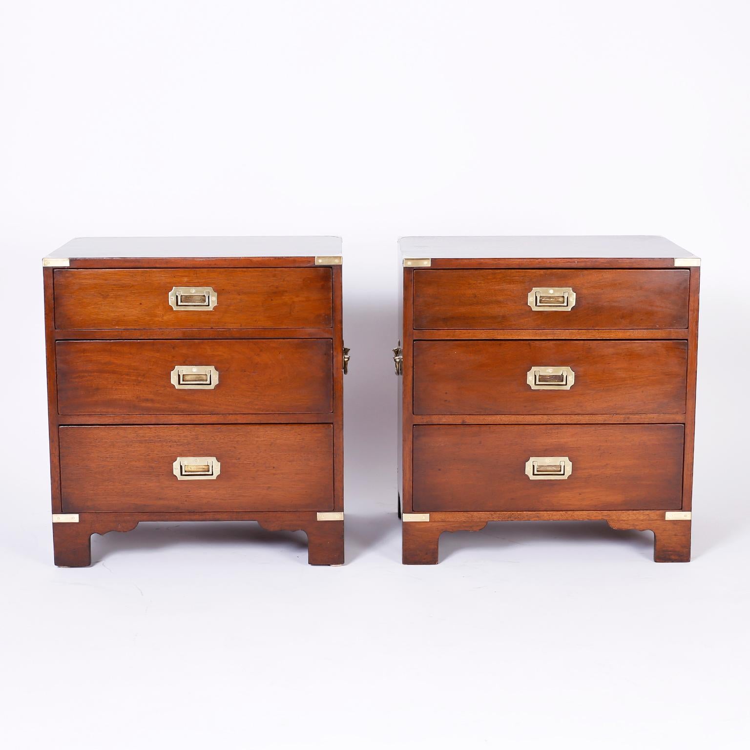 Handsome pair of midcentury campaign style three drawer nightstands crafted in mahogany with brass hardware and bracket feet.