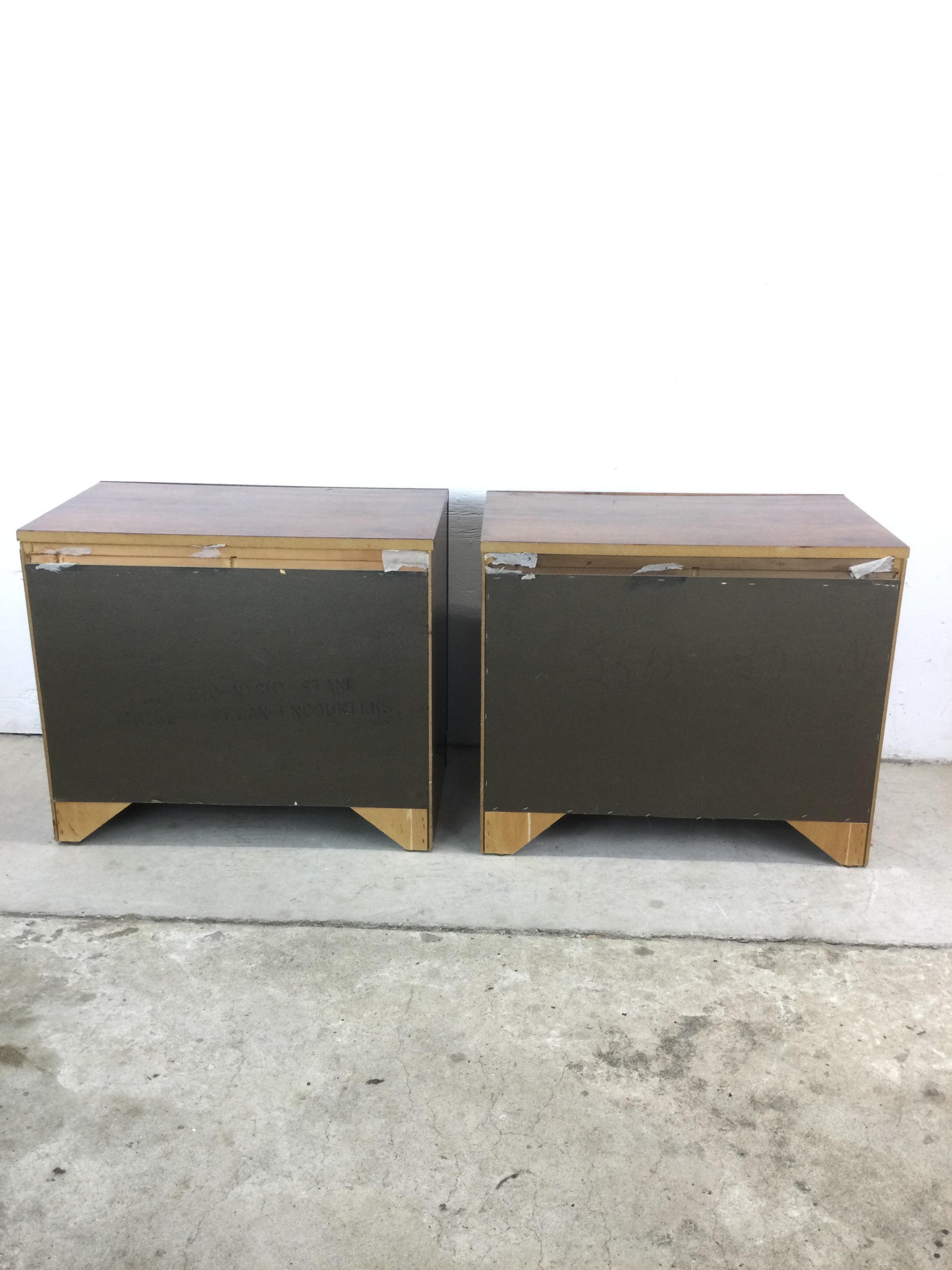 This pair of mid century campaign style nightstands. by Bassett Furniture feature hardwood construction, beautiful oak veneer with original finish, two dovetailed drawers with brass accented trim and hardware, and a plinth style base.

Matching
