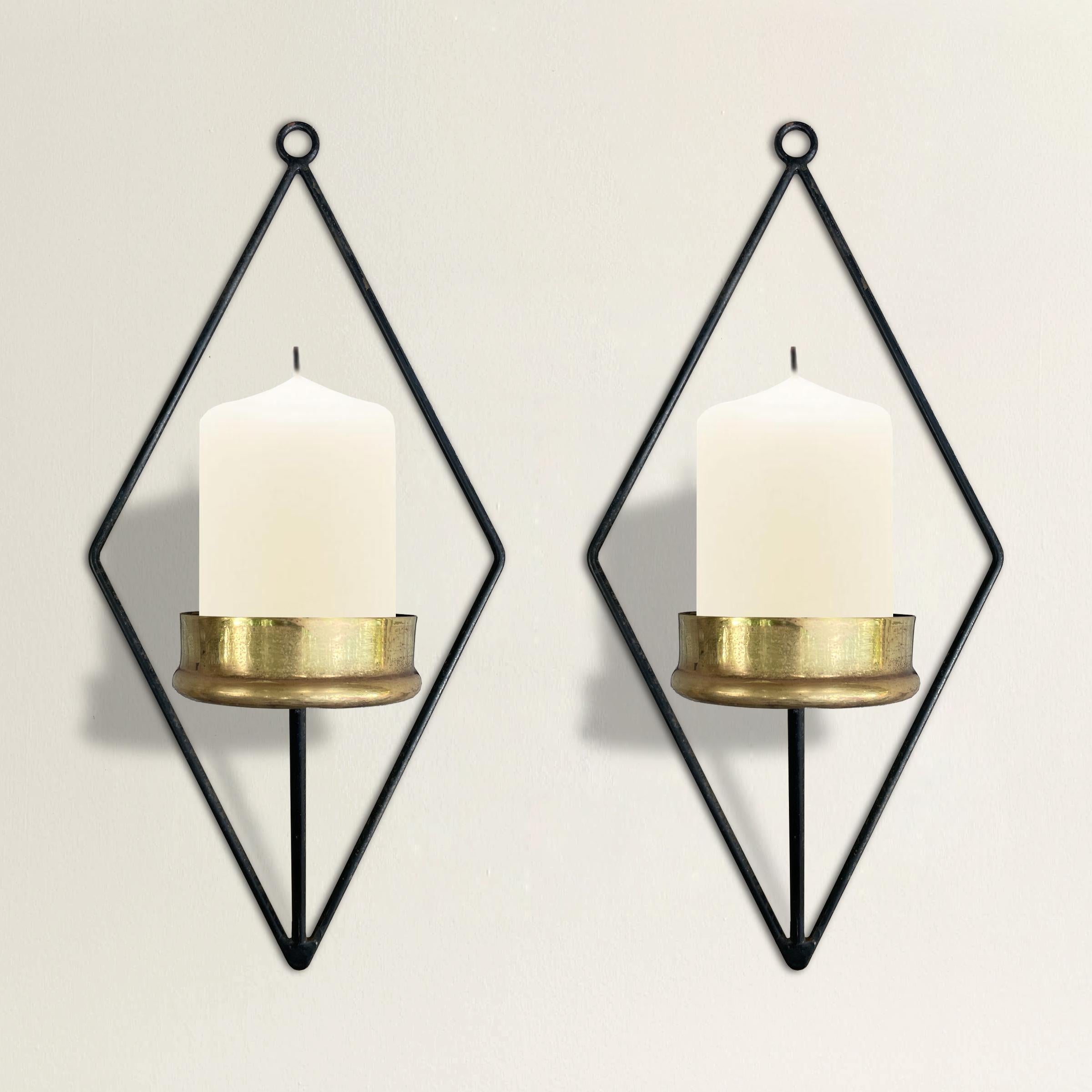 A pair of chic mid-20th century Italian candle sconces with simple steel diamond-form frames and single arms supporting brass candle cups. The sconces can accommodate pillar and taper candles.