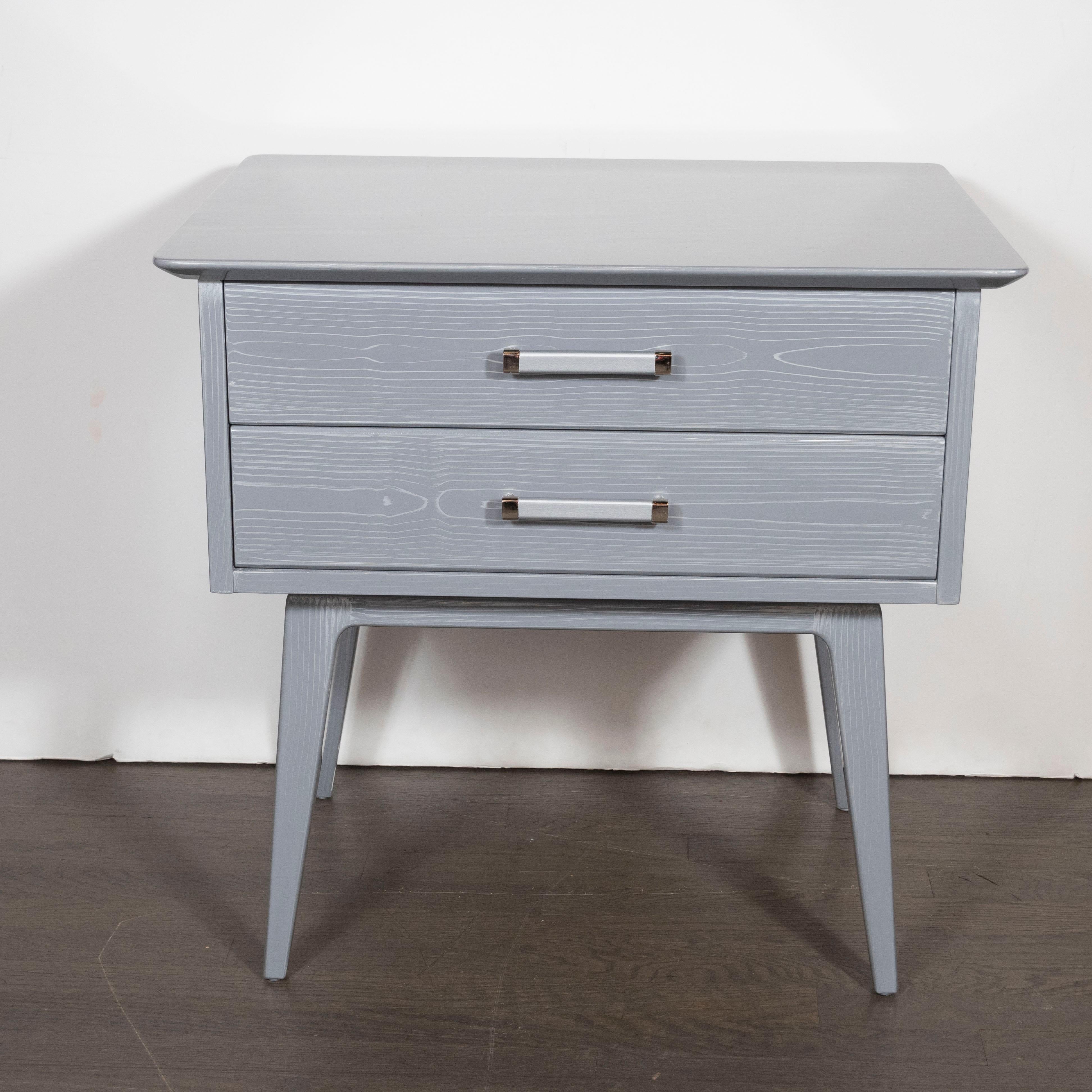 This stunning pair of Mid-Century Modern nightstands/ end tables were realized by John Stuart Inc. in the United States, circa 1950. They offer a volumetric rectangular body; slightly cantilevered top with rounded edges; splayed tapered legs; and