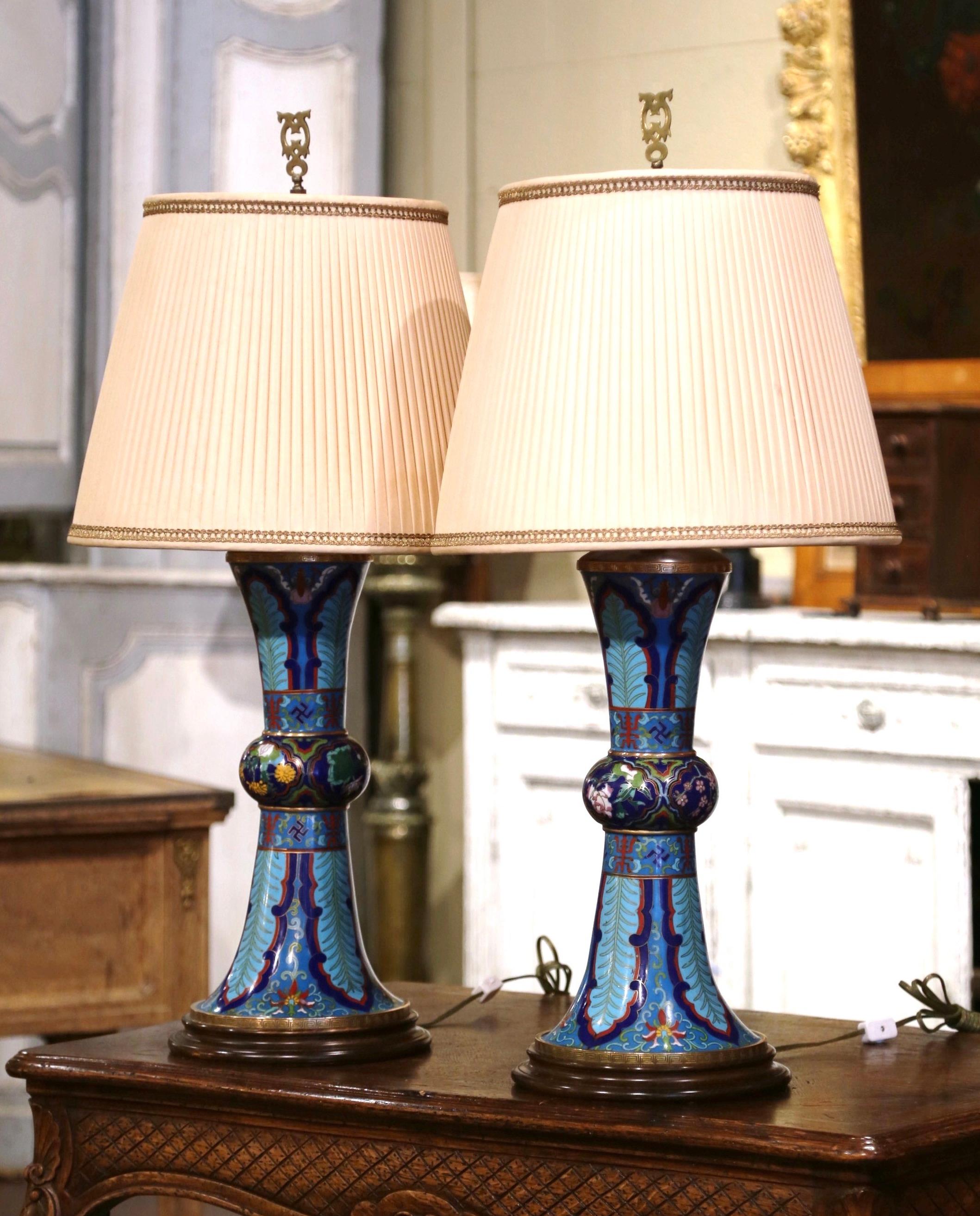 Dress a buffet or a console with this colorful pair of oil shaped cloisonne table lamps; created in China circa 1950, each tall piece sits on a carved mahogany base and features floral and leaf motifs in the cloisonné technique (decorative work in