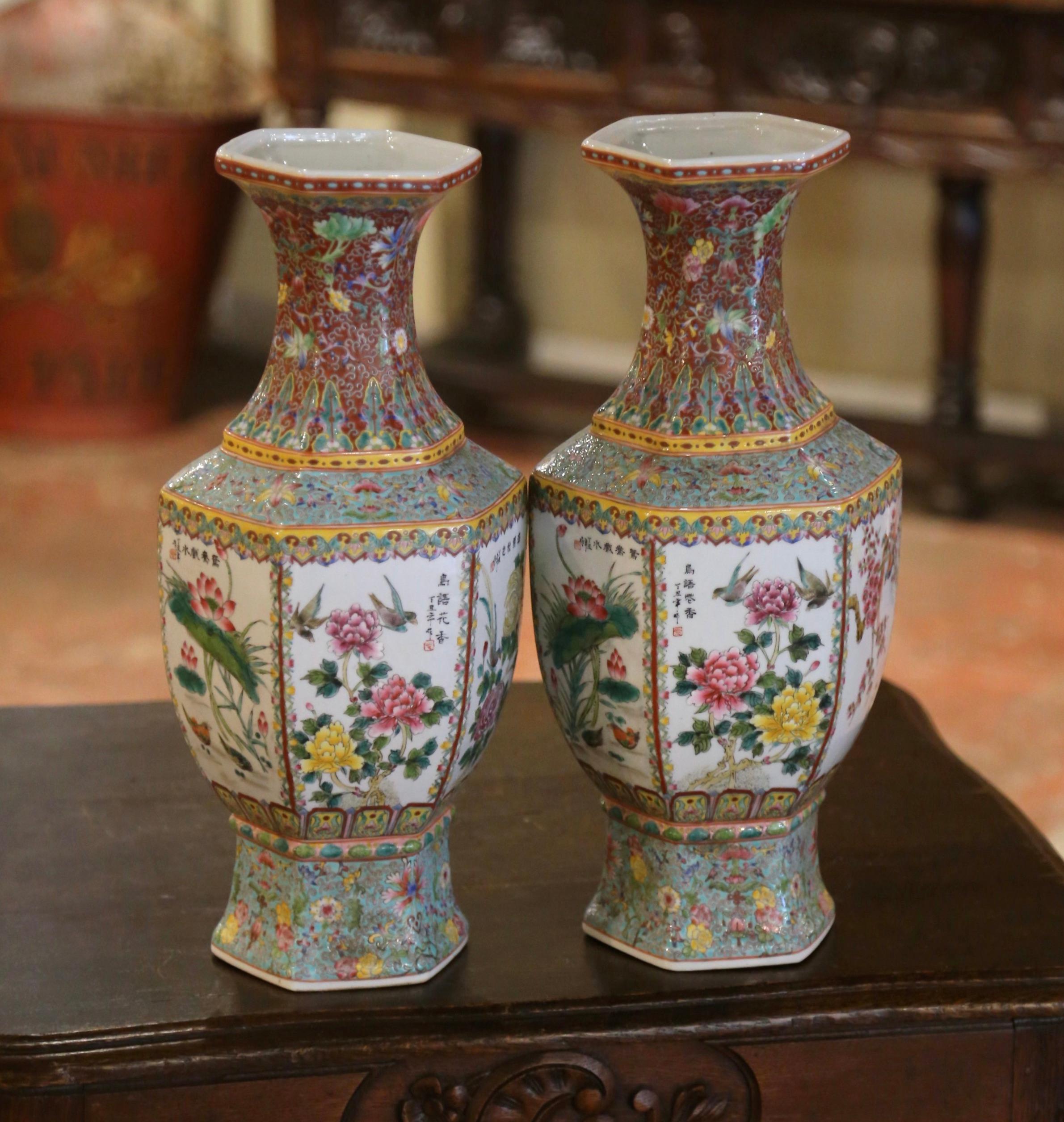 These elegant colorful Famille Rose vases were created in China circa 1950. Standing tall, the large vessels feature a flared rim and hexagonal body. Each body is adorned with vibrant floral and peacock motifs, characteristic of traditional Chinese