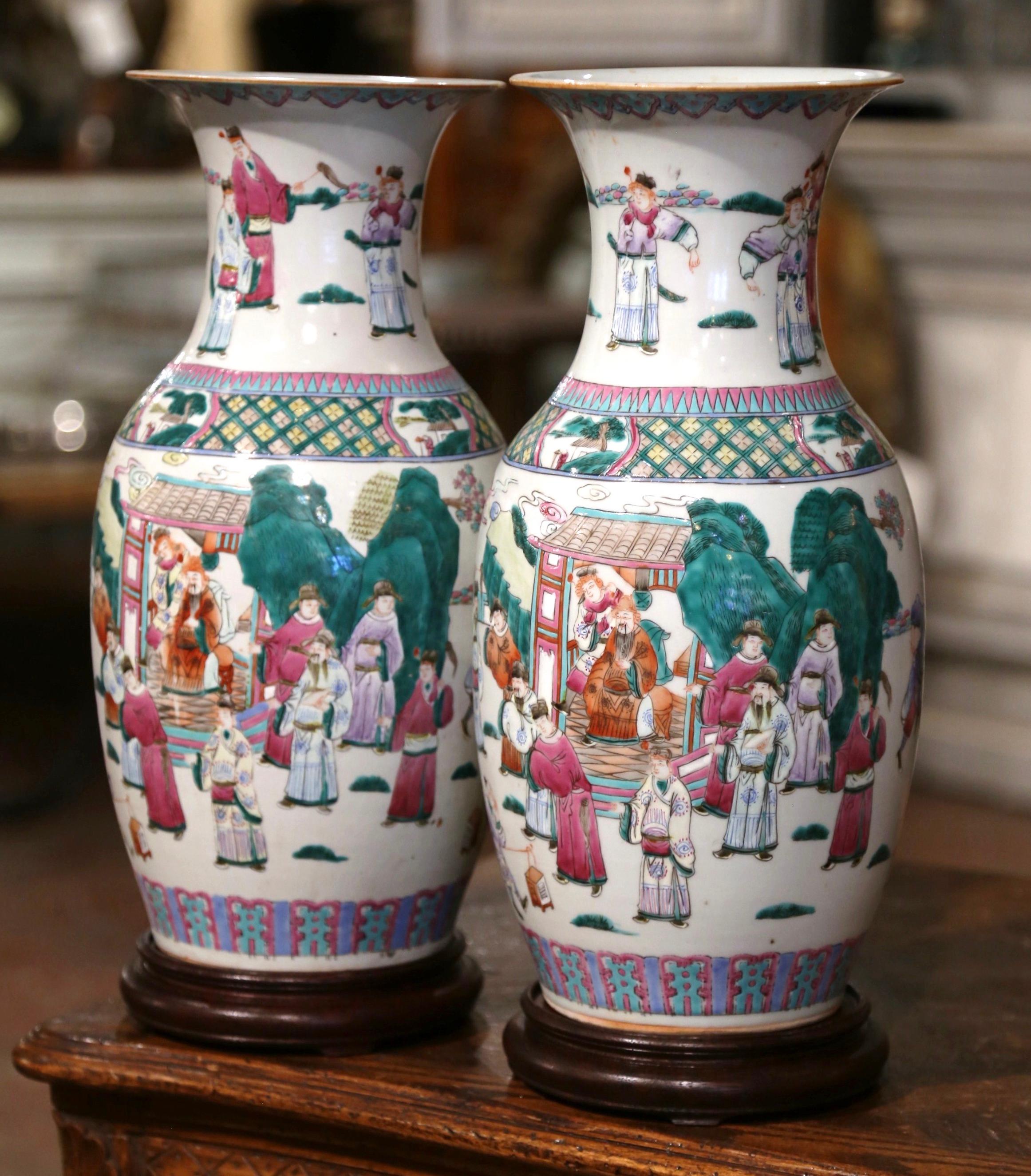 These elegant colorful antiques Famille Rose vases were created in China circa 1950. Standing on platform bases, the large vessel feature a flared rim and tapered body. Each body is decorated with hand painted figural scenes and geometric trim