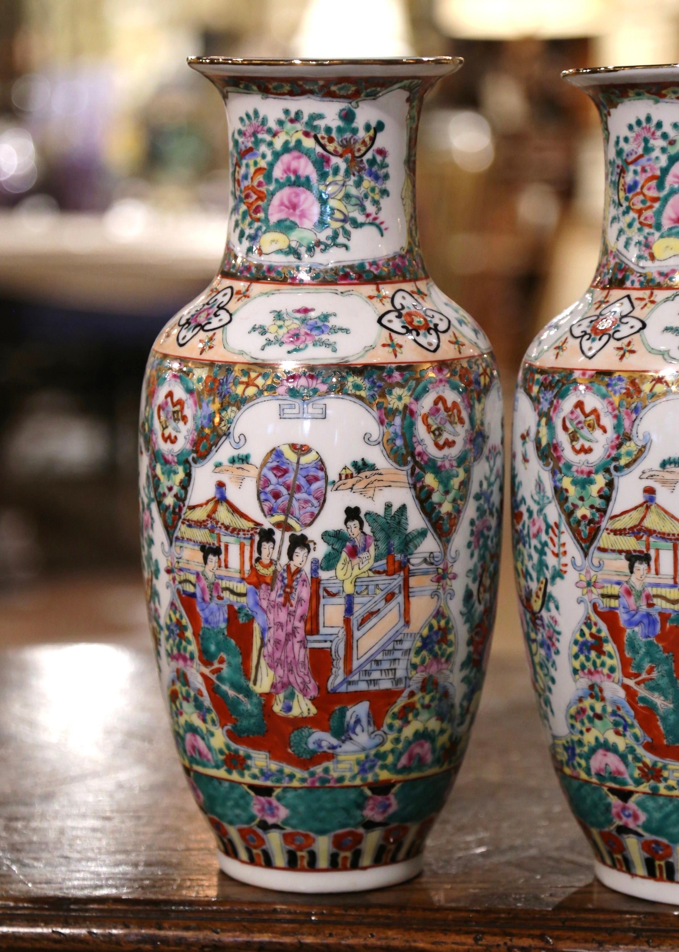 These elegant rose medallion porcelain vases were created in China circa 1960; made of porcelain and embellished with gilt accents throughout, each vase is decorated with hand painted polychrome enameled flowers, courtly figural scenes, and