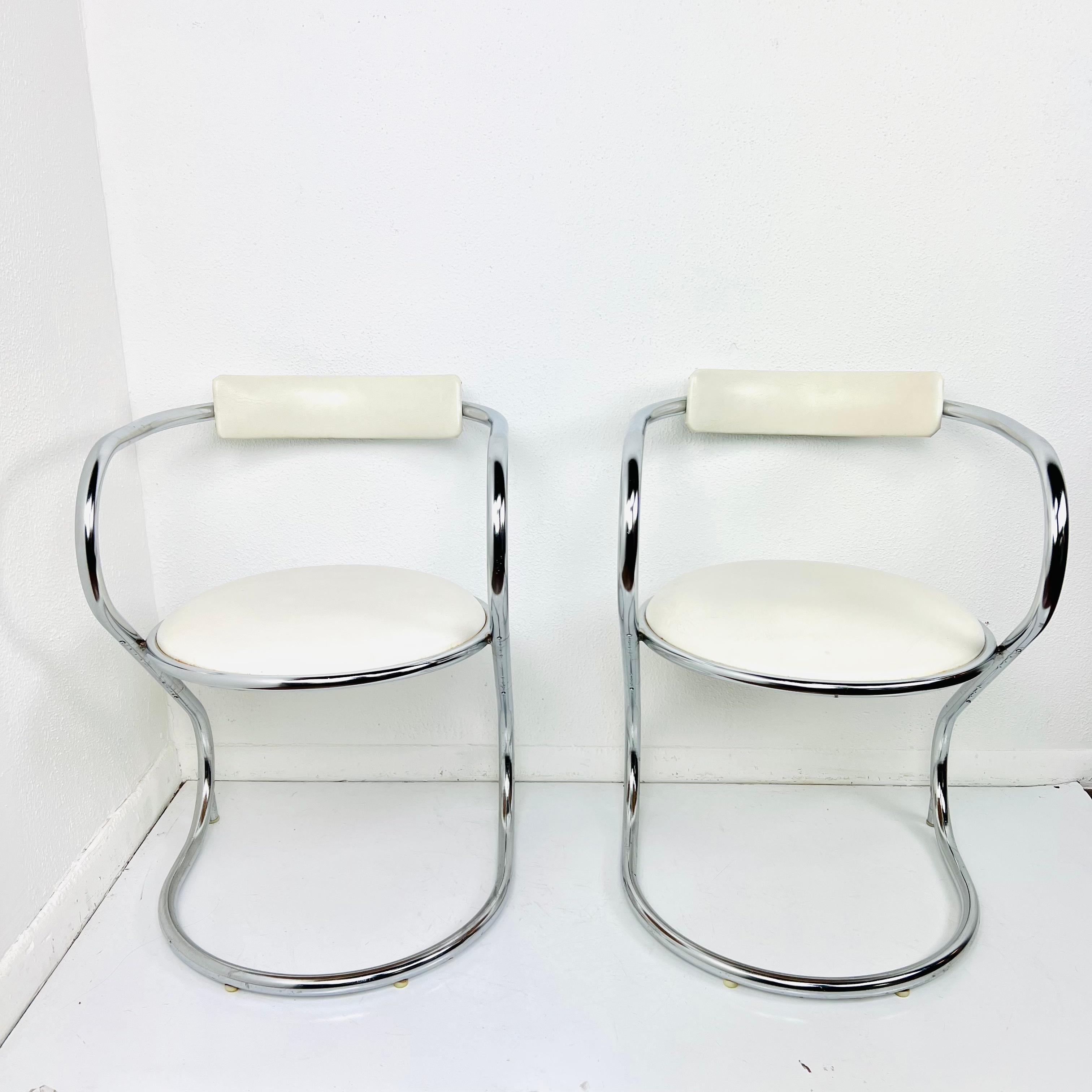 Chic pair of chairs featuring cantilever design, curvaceous steel tube bases, and rounded seats with minimal bar backrests to keep the Silhouette simple and clean. Upholstered in white vinyl. Condition is good, with some minor pitting to chrome and