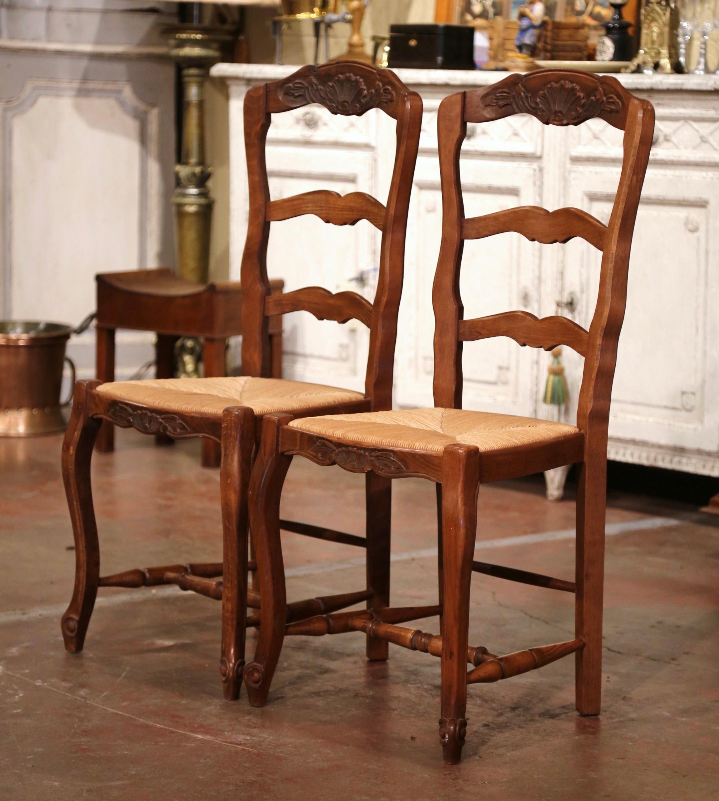 Decorate a bedroom with this elegant pair of antique chairs. Hand carved from beech wood in Normandy France circa 1930, each chair stands on front cabriole legs with bottom stretcher, over a scalloped and bowed apron. The three-ladder back features
