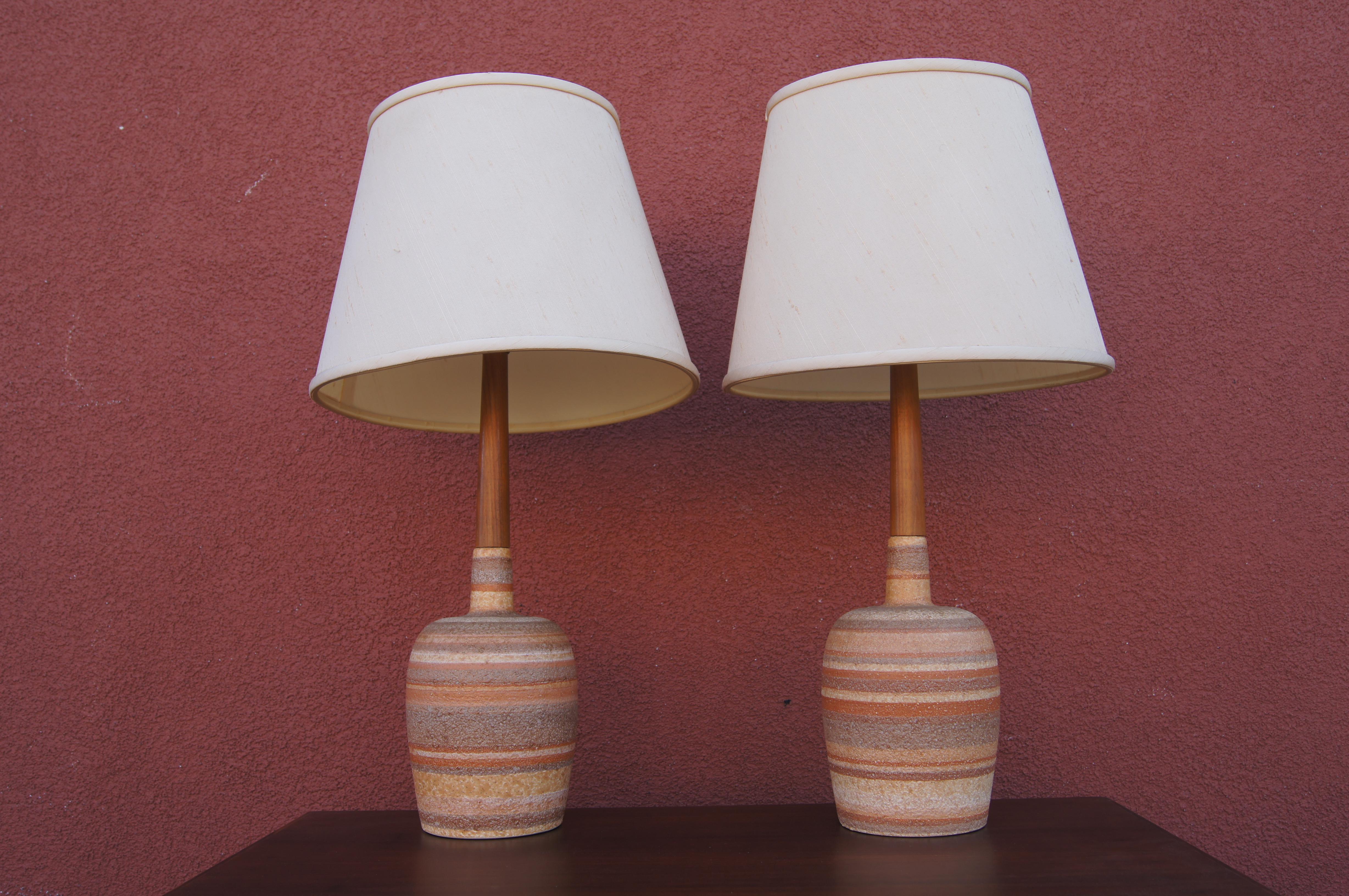 This sweet pair of midcentury Danish tables lamps features bases of unglazed striated ceramic from which rise narrow columns of teak to support the socket.

Measurement below is to the top of finial. Shades included.