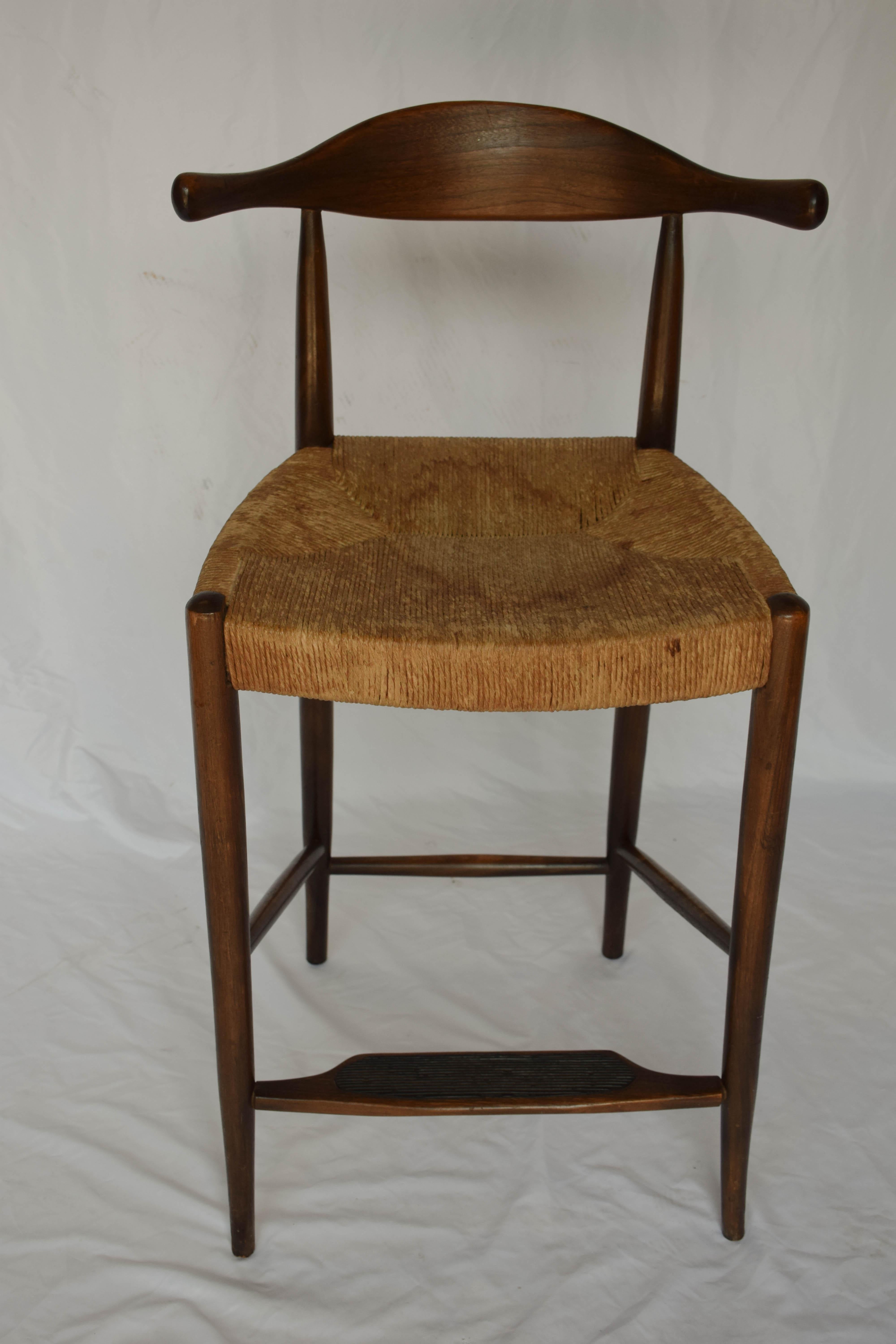 This is a pair of midcentury Danish Modern Hans Wegner style cow horn (OX Bow) counter height bar stools. Created between 1950 and 1960, the stools are made of teak wood and have a rush seat. The base has a asymmetrical design with a rubber pad on