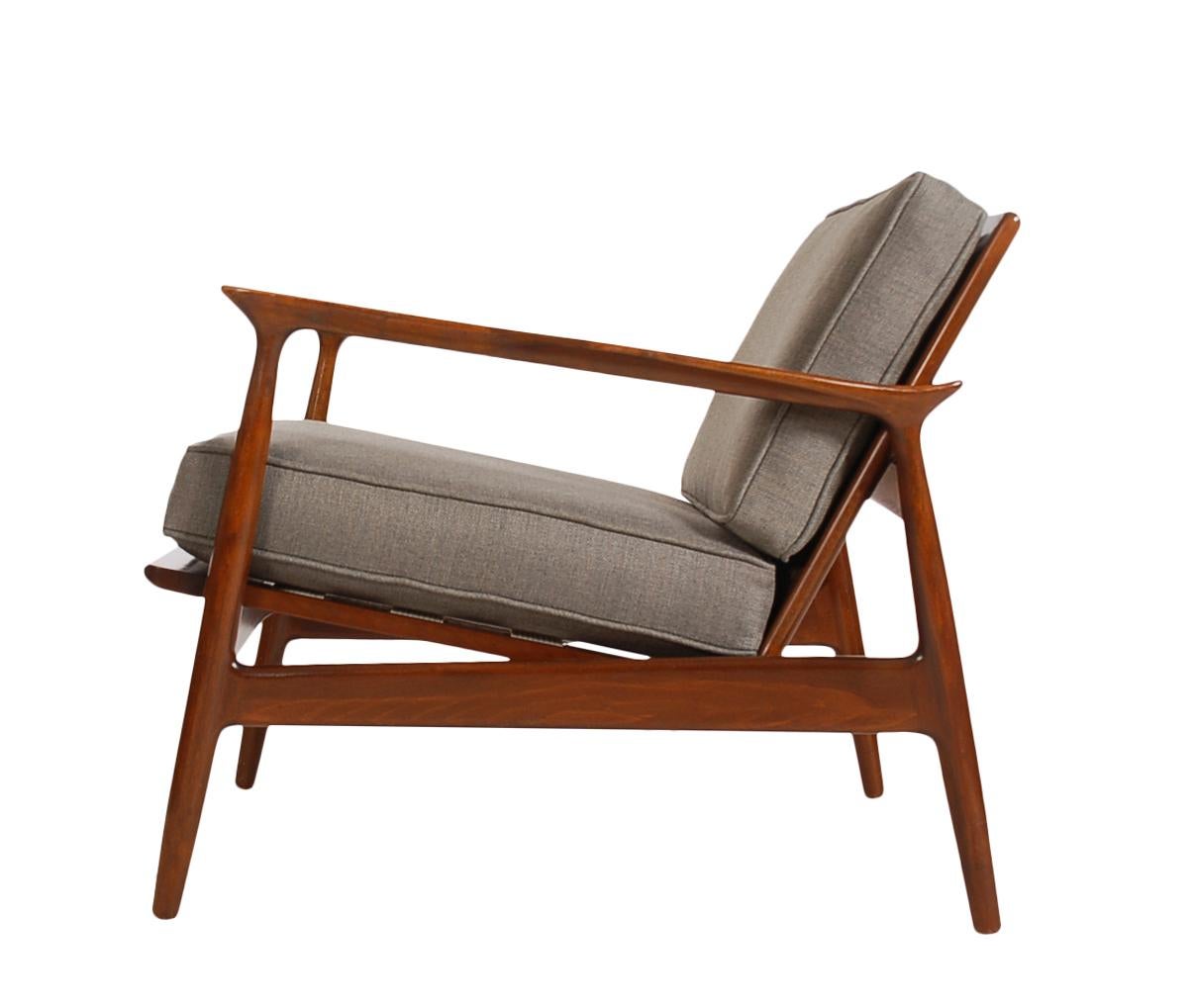An early example IB Kofod Larsen's work; these lounge chairs have beautiful design lines from the 1950's. These feature solid walnut frames, raffia backs, new upholstery, and new seat webbing. Stamped made in Denmark.