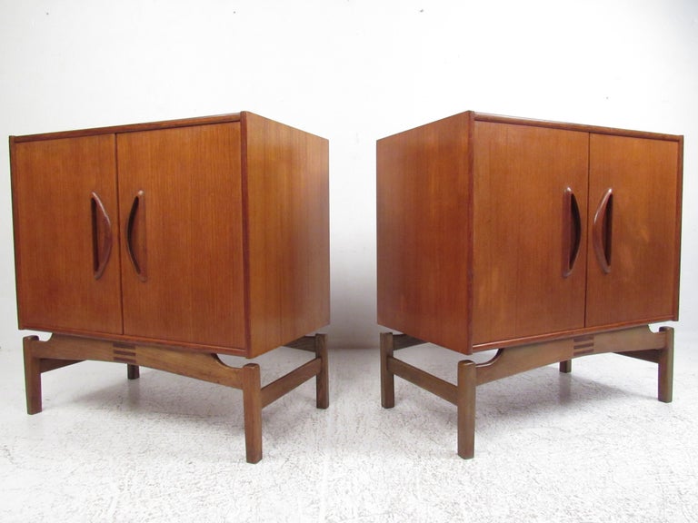 This beautiful pair of vintage modern cabinets feature unusual carved pulls and a sculpted base. The sleek design offers plenty of room for storage within its large open compartment. A finished back, elegant wood grain, and a rich teak finish show