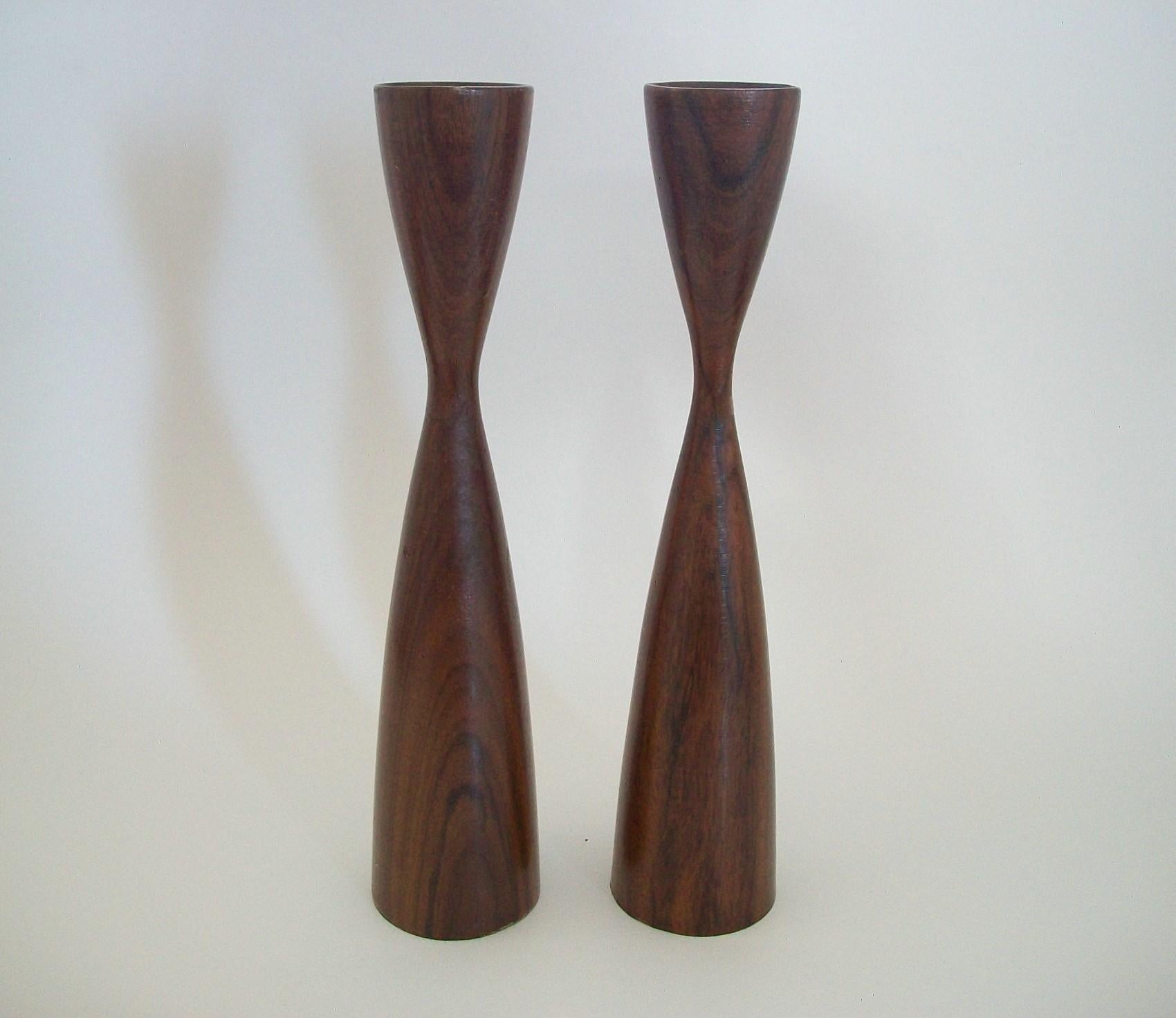 Pair of midcentury Danish teak candlesticks - featuring an elegant modern design in a medium brown finish - each signed on the base (unidentified maker) - Denmark - circa 1960s.

Excellent vintage condition - minor scuffs - no loss - no damage -