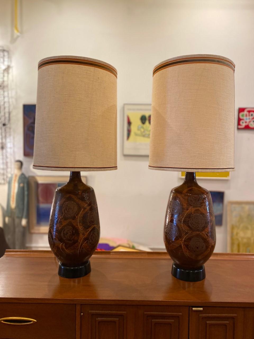 Beautiful pair of midcentury ceramic drip glazed table lamps. The pair includes lamp shades and together bring that MCM feel to your decor. Both lamps present a beautiful glazed design that permeates with hues of dark reddish hues in variant shades
