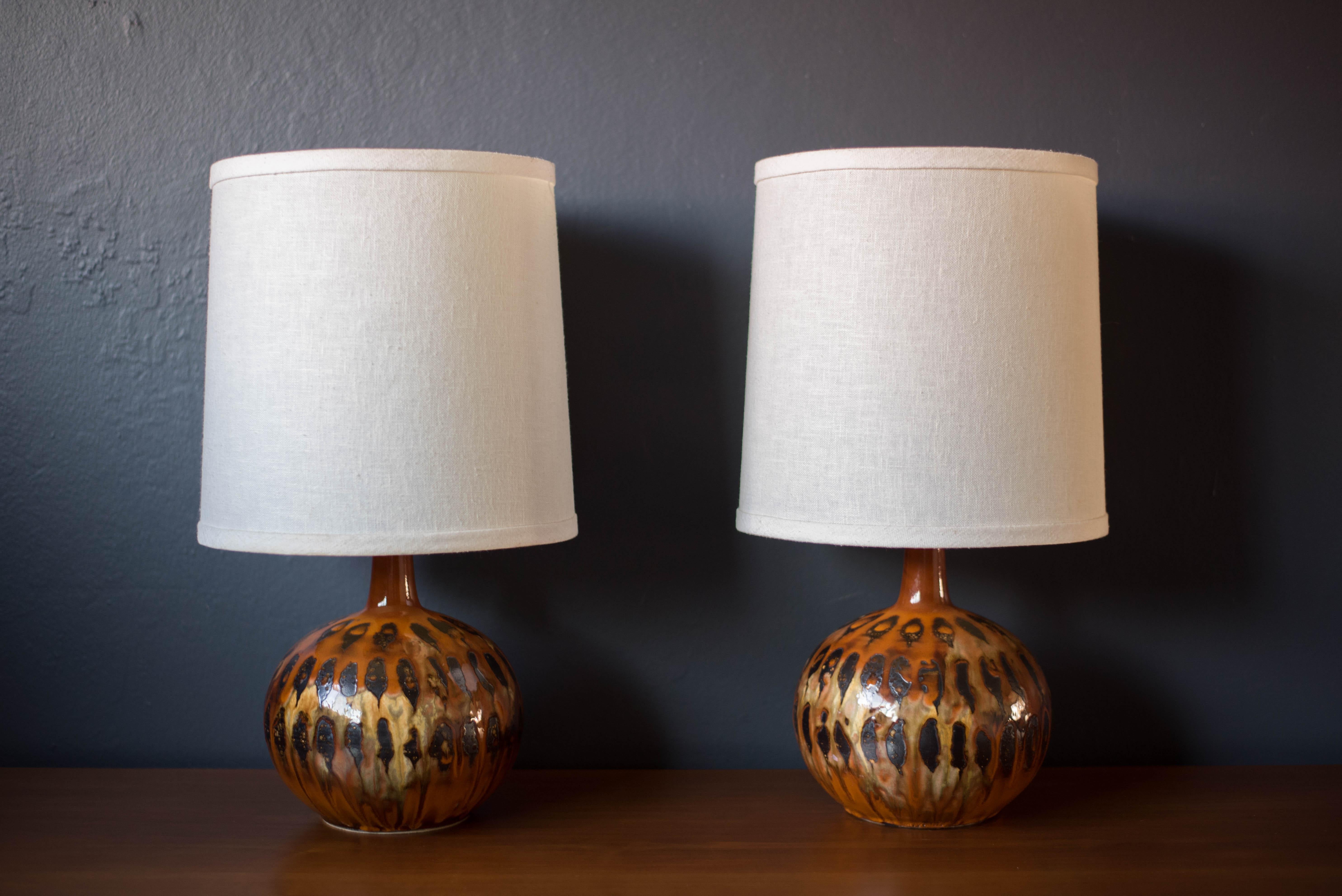 Vintage ceramic pottery lamps manufactured in the US. This set features a vibrant pattern of orange, neutral, and black tones in a drip glazed finish. Functions with a three way switch to emit a soft or brighter glow. Linen drum shades are