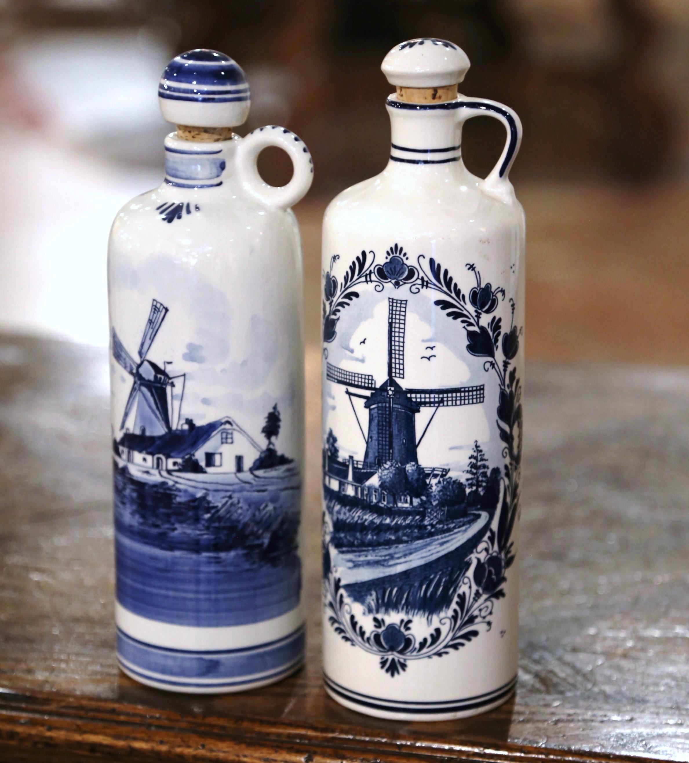 Decorate a shelf or kitchen counter with this pair of antique Delft olive oil containers. Crafted in Holland circa 1960, each tall vase is dressed with a cork top, and features traditional hand painted blue and white Delft motifs including a wind