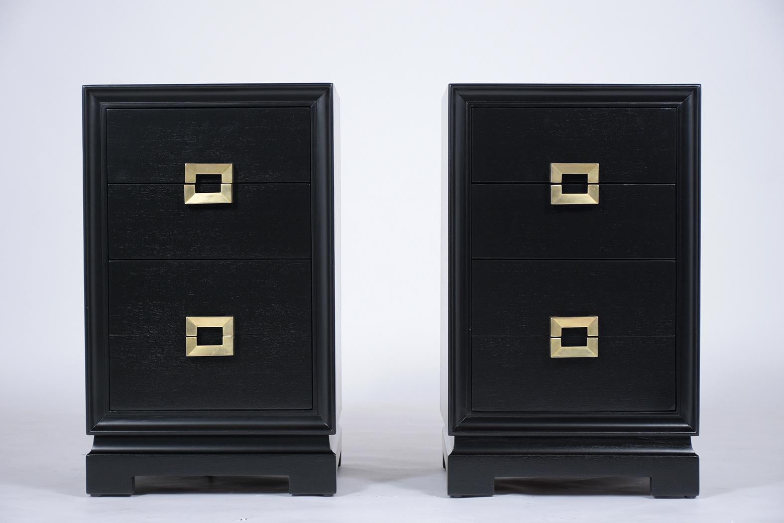 A pair of midcentury nightstands finely crafted out of mahogany wood and features a newly elegant ebonized stain and satin lacquered finish. The end tables also have two drawers with newly polished eye-catching brass handles and rest on a pedestal