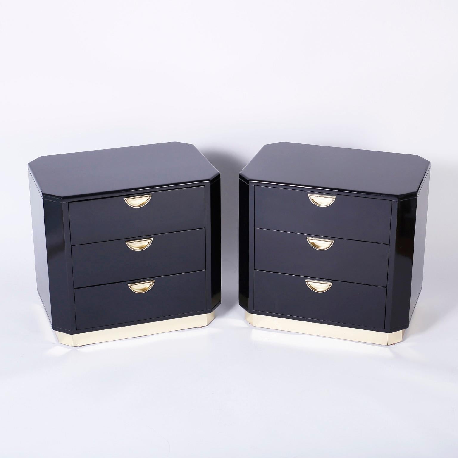 In voque pair of three drawer black lacquered nightstands with a sleek refined form, inset brass pulls and a brass block foot. Signed John Widdicomb in a drawer.
