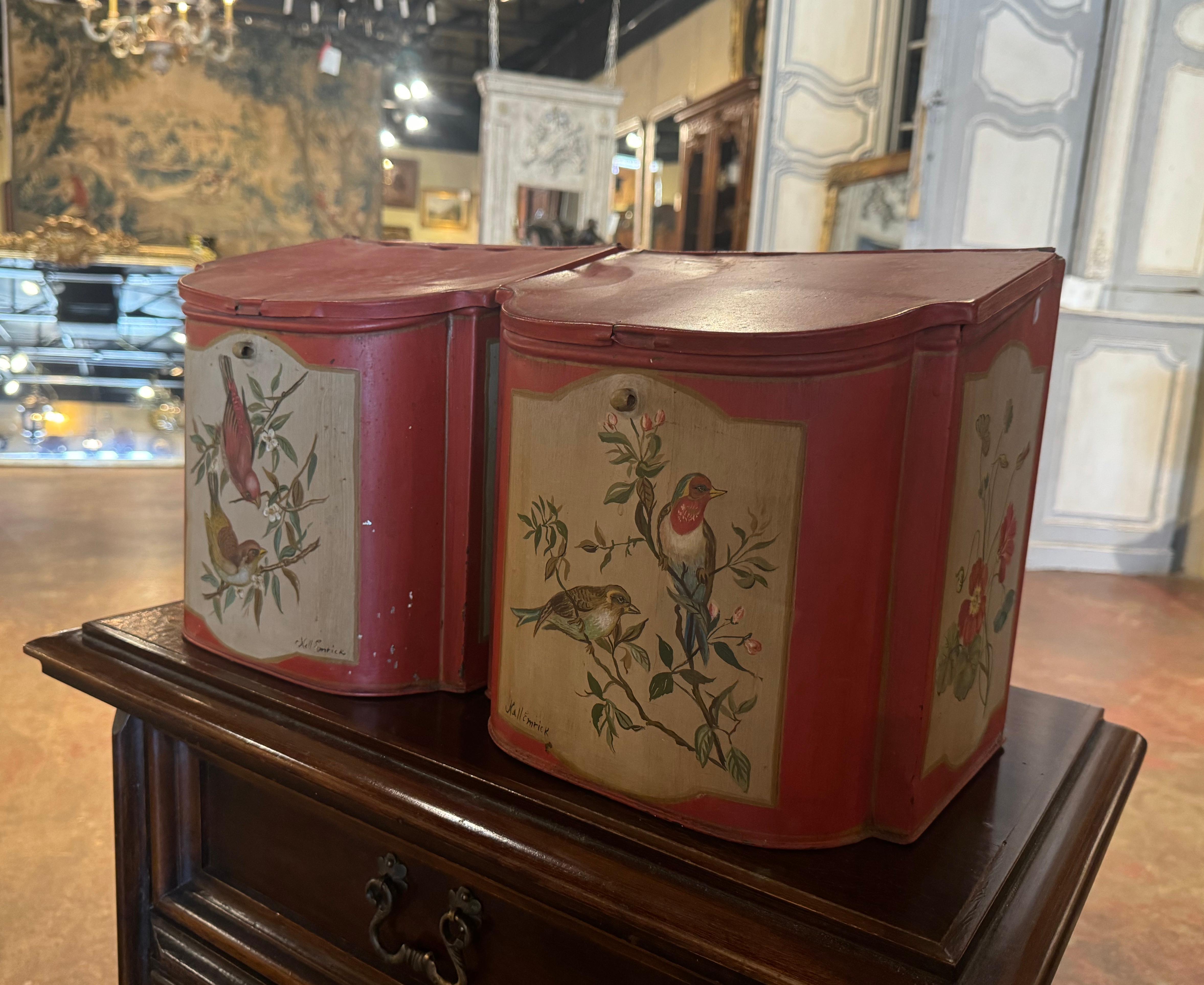 Decorate a kitchen cabinets with this pair of colorful tea boxes. Crafted in England circa 1950, and built of tinned metal, each decorative box with attached lid, is hand painted with bird, floral and leaf motifs. The boxes are in excellent