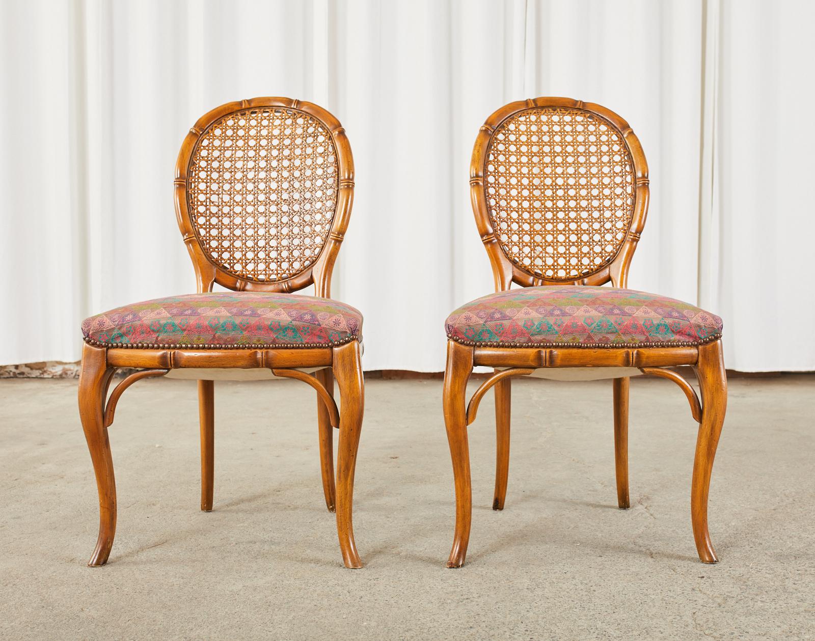 Hollywood regency pair of carved faux bamboo dining chairs made in the mid-20th century. The chairs feature a round bamboo carved back inset with cane. The seats are upholstered with a late 20th century geometric fabric bordered by brass tack nail