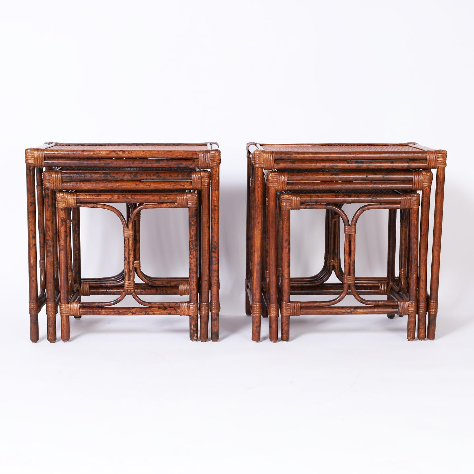 Rare pair of British colonial style nests of tables or stands each with faux bamboo frames wrapped with reed and grass cloth panels on the table tops.


