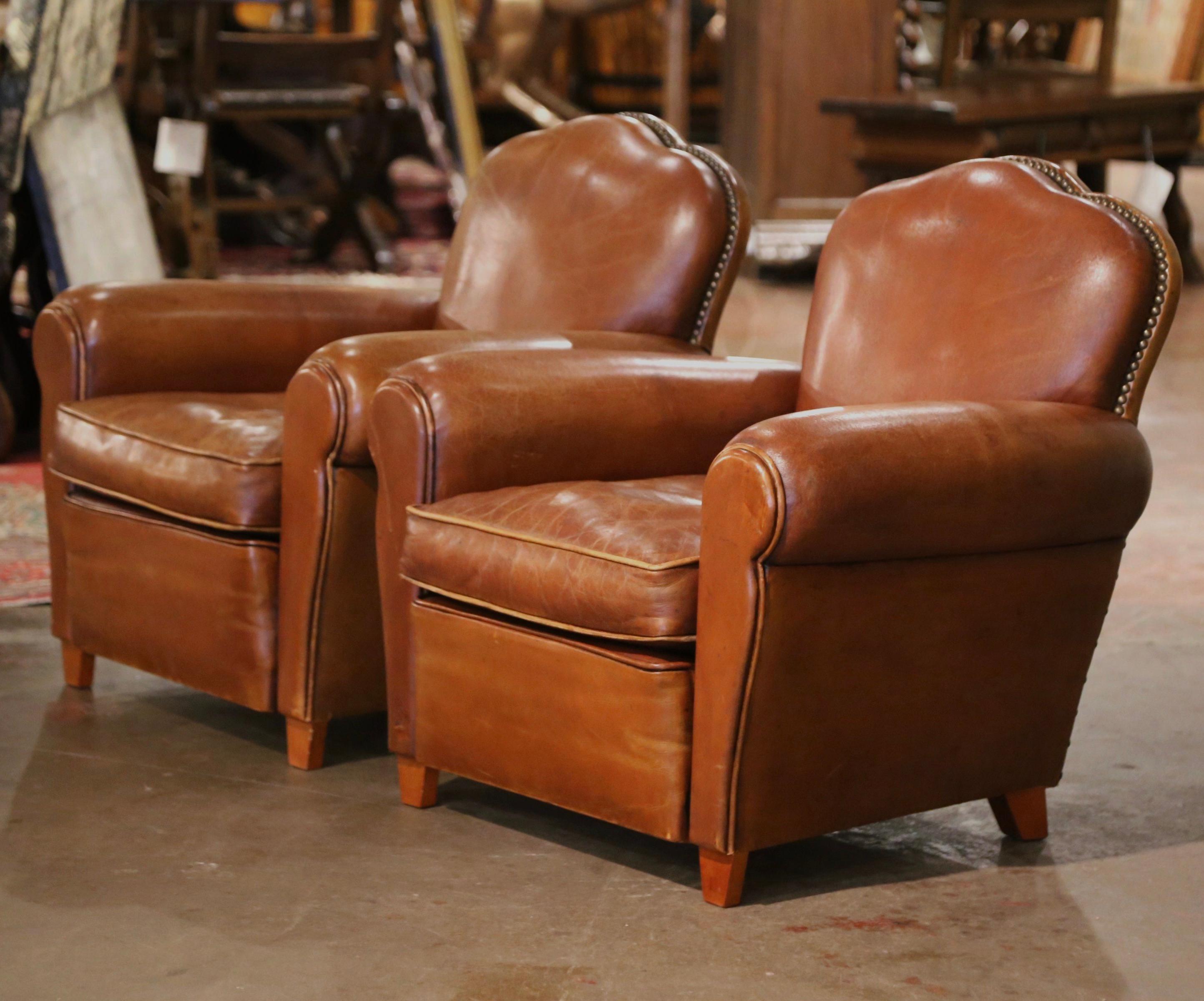 These Classic, antique Art Deco club chairs were crafted in France, circa 1970. The stately chairs feature wide, rounded armrests, a pitch back with an arched top shape, and tapered wooden feet at the base. The Classic, masculine French chairs are
