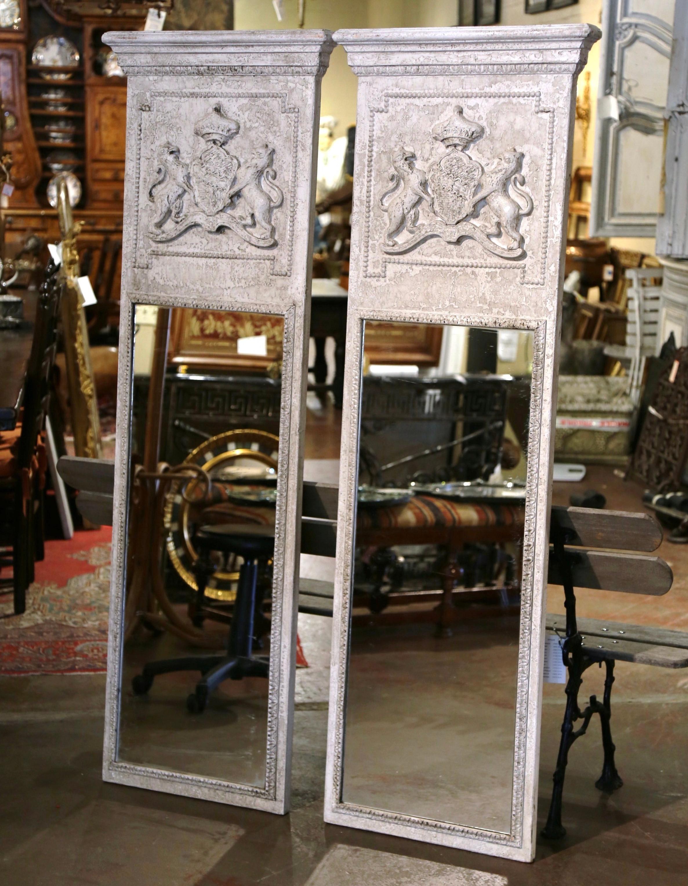 Decorate a living room, or an entry with this elegant pair of colorful antique trumeaux mirrors. Crafted in France, circa 1950, each tall trumeau is dressed at the pediment with a thick crown. Each wall piece features a hand carved heraldic crest in