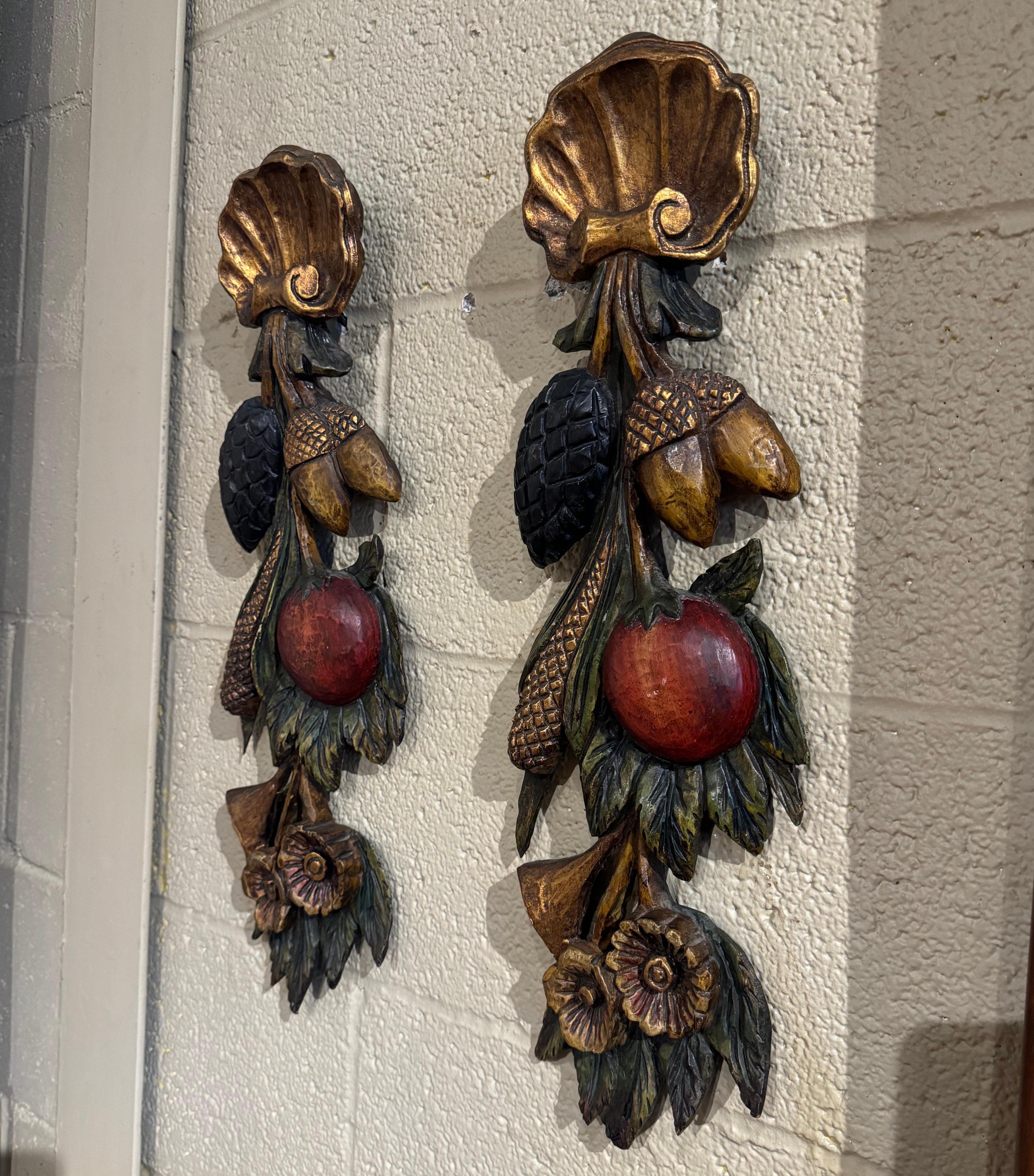Decorate a dining room or living room wall with this elegant pair of antique polychromed wall sculptures. Hand carved in France circa 1950, each trophy features a traditional a gilt shell at the pediment, and carved foliage and leaf motifs