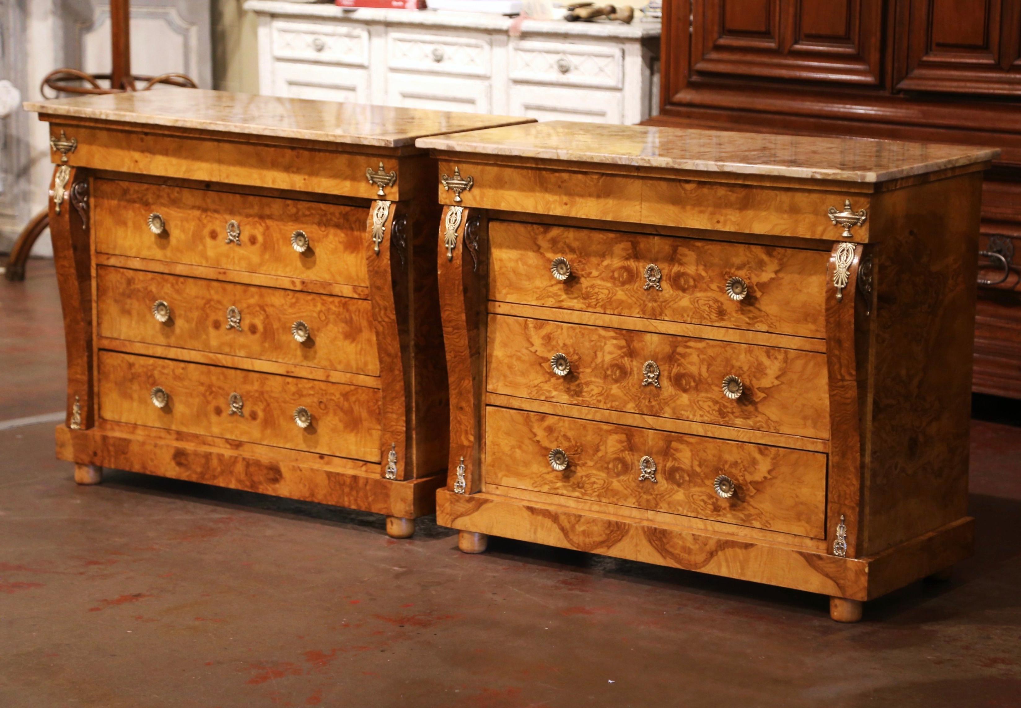 Crafted in France, circa 1960, each chest built of burl elm, sits on bun feet over a straight plinth apron. Decorated with scrolled corner posts dressed with bronze mounts, each cabinet with projecting top frieze features three drawers across the