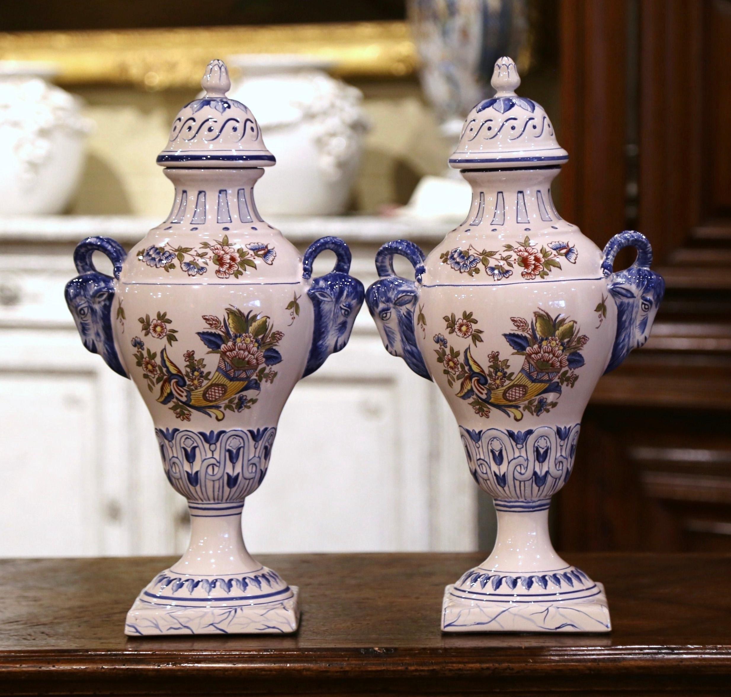 These elegant, antique urns were created in Luneville, France, circa 1970. The tall ceramic vases stand on square bases over a bombe body decorated with ram head handles, and embellished with a cone shape lid. Each colorful piece is hand painted