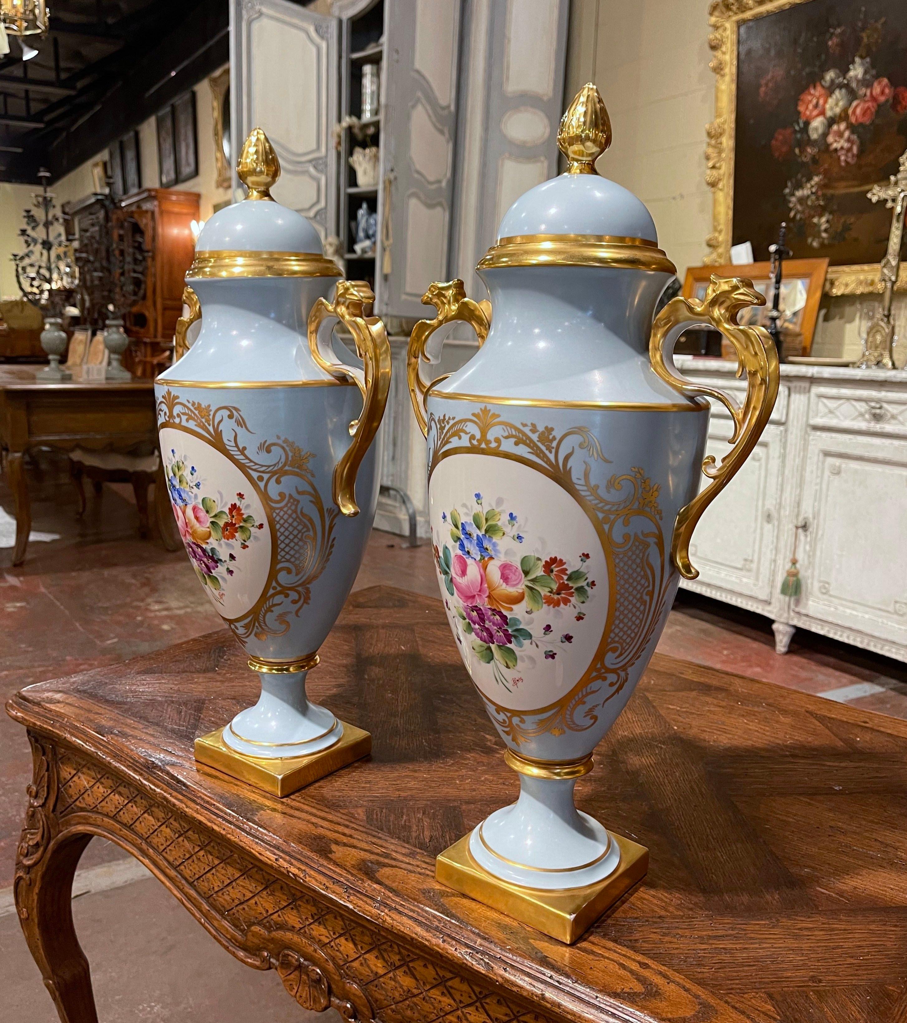 Bring a little color into your home with this pair of elegant, antique porcelain vessels. Crafted circa 1950, each vase is dressed with a dome lid and intricate side handles with bird figure. Both colorful urns are stamped on the bottom 