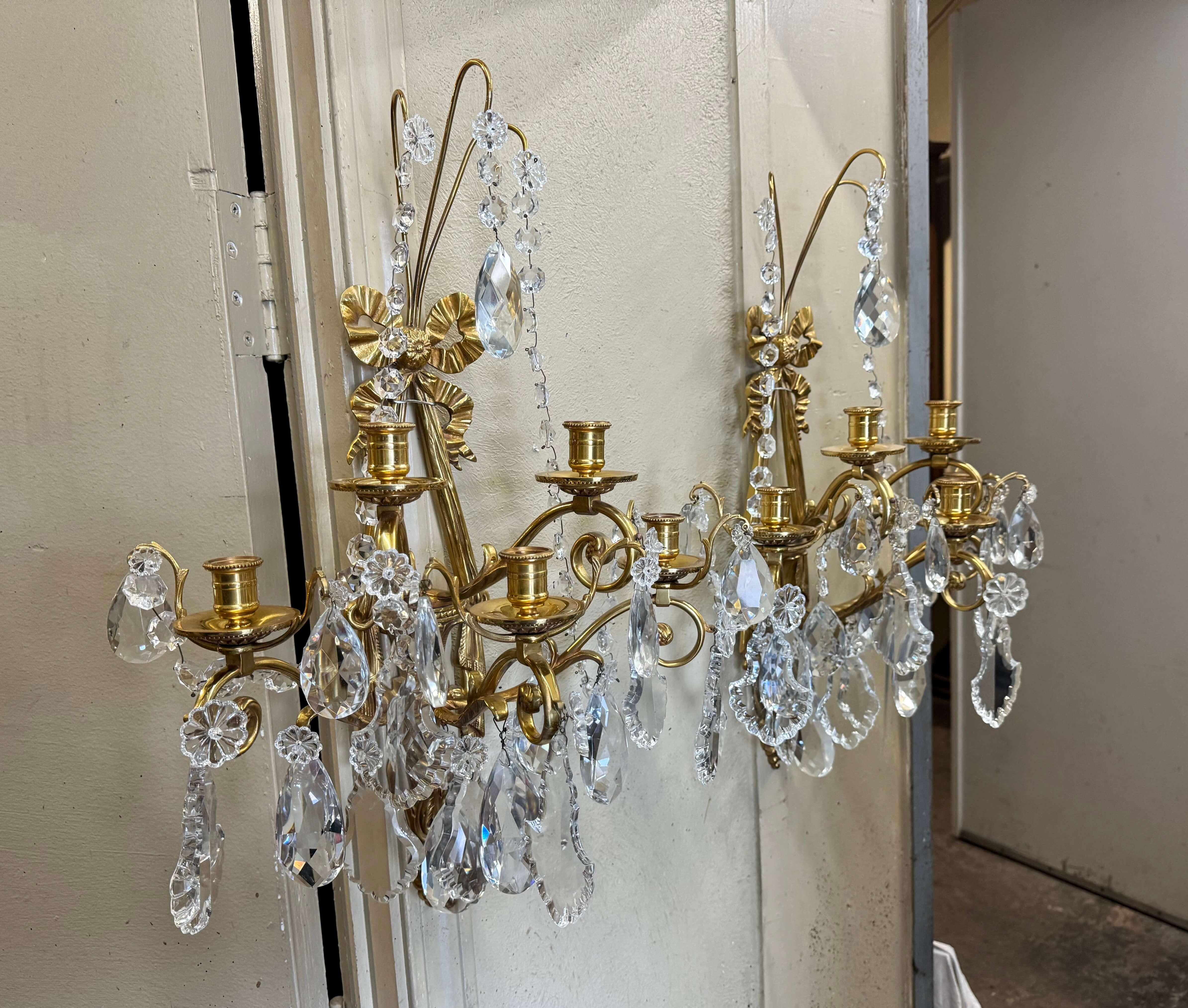 Décorez une salle d'eau ou un salon avec cette élégante paire d'appliques dorées anciennes. Fabriqué en France, vers 1960, chaque luminaire présente le traditionnel nœud de ruban Louis XVI au fronton, des motifs de guirlandes sur les côtés et un