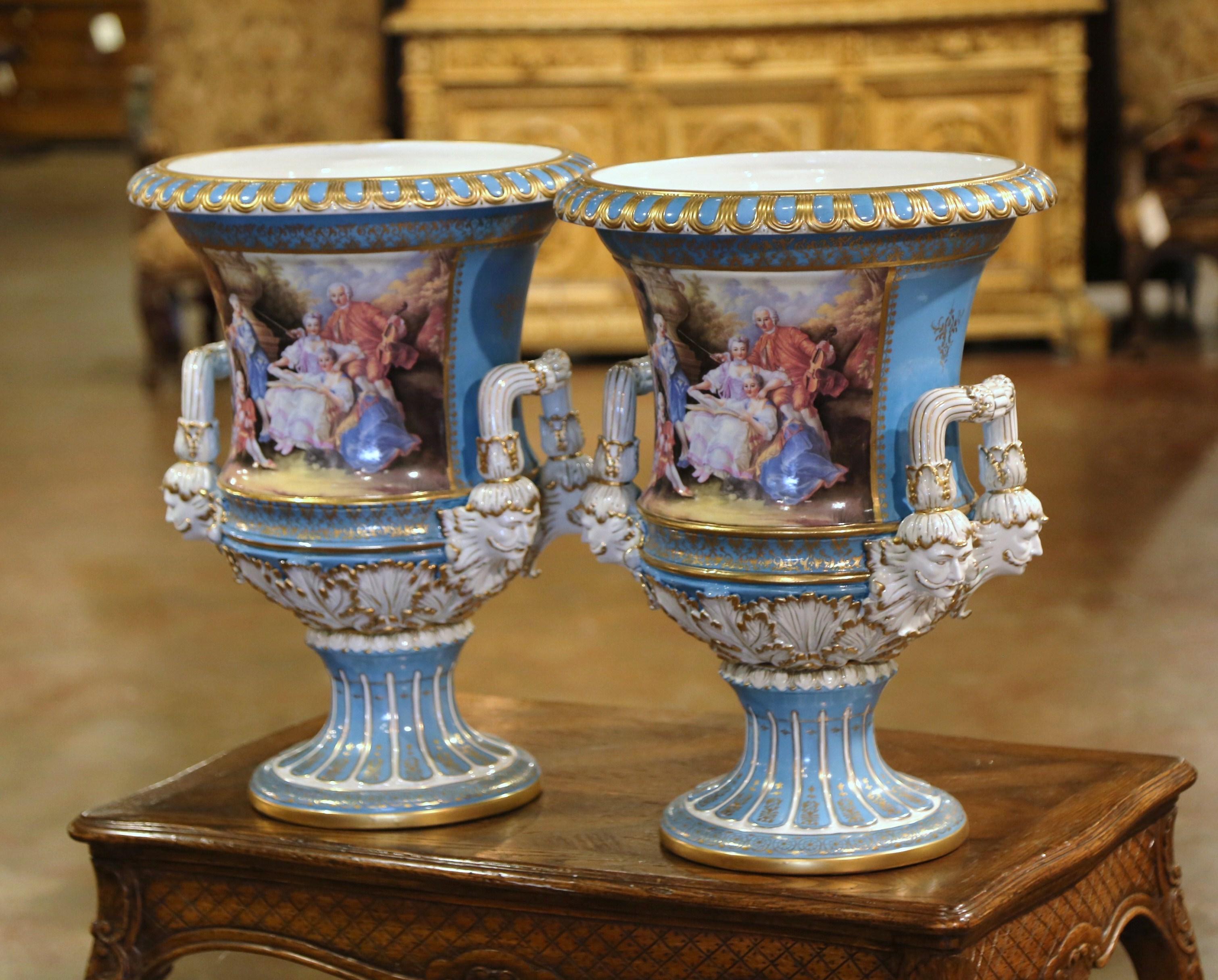 Decorate a buffet or a mantel with this large pair of antique porcelain urns. Crafted in France circa 1950 in the manner of Sevres, each colorful vase is mounted on a circular base decorated with acanthus leaf motif in high reliefs and embellished