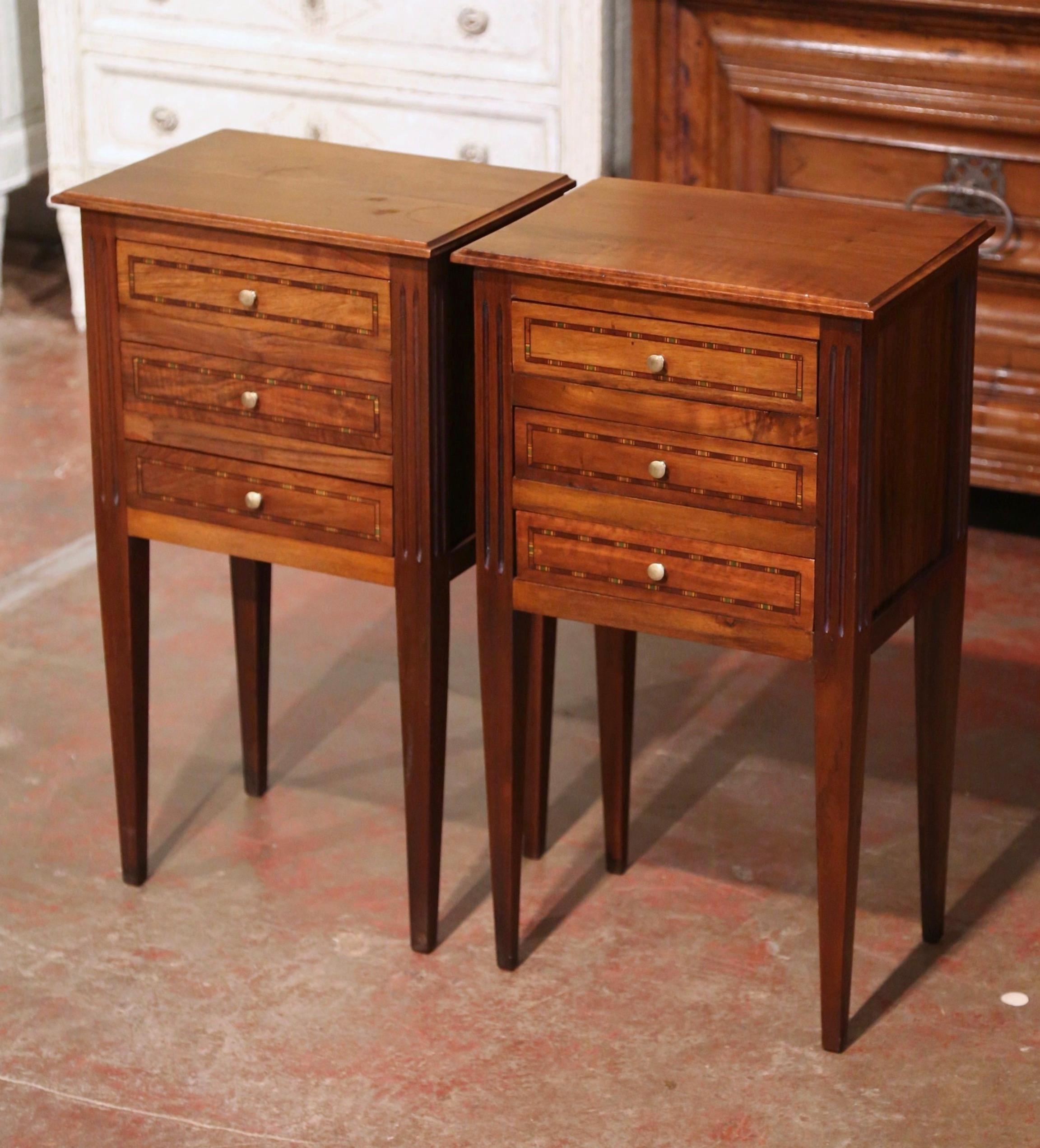 Decorate a bedroom with this elegant pair of antique bedside tables. Crafted in France circa 1950, each nightstand stands on four tapered legs, and features three drawers decorated with polychrome inlay fillet in contrasting finish, and further