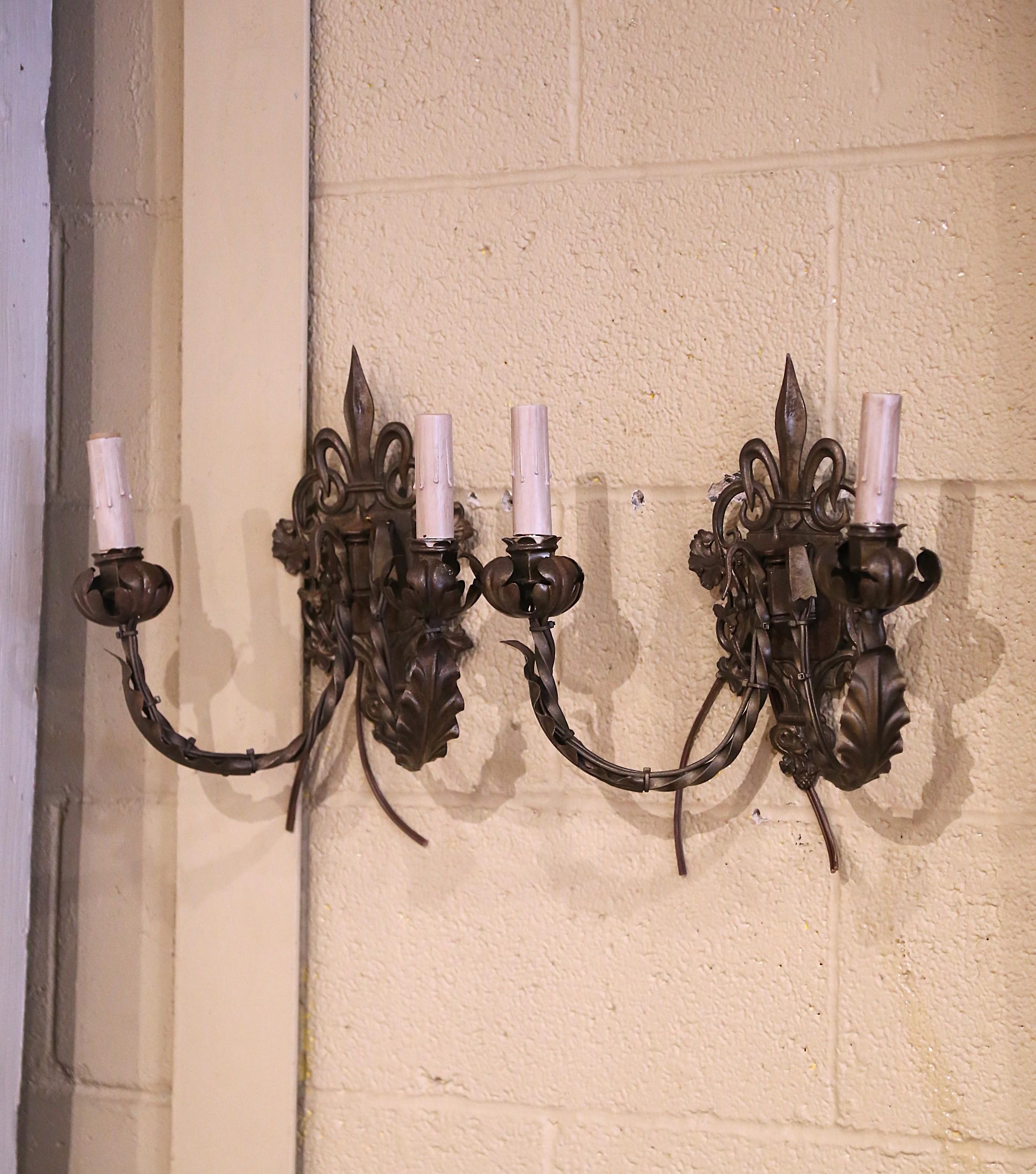 Vesti una toilette o un ingresso con questa elegante coppia di applique. Creato a Parigi, in Francia, intorno al 1950, ogni apparecchio a due luci è decorato con un motivo Fleur-de-Lys sul frontone. L'intricata lavorazione del metallo a tortiglione