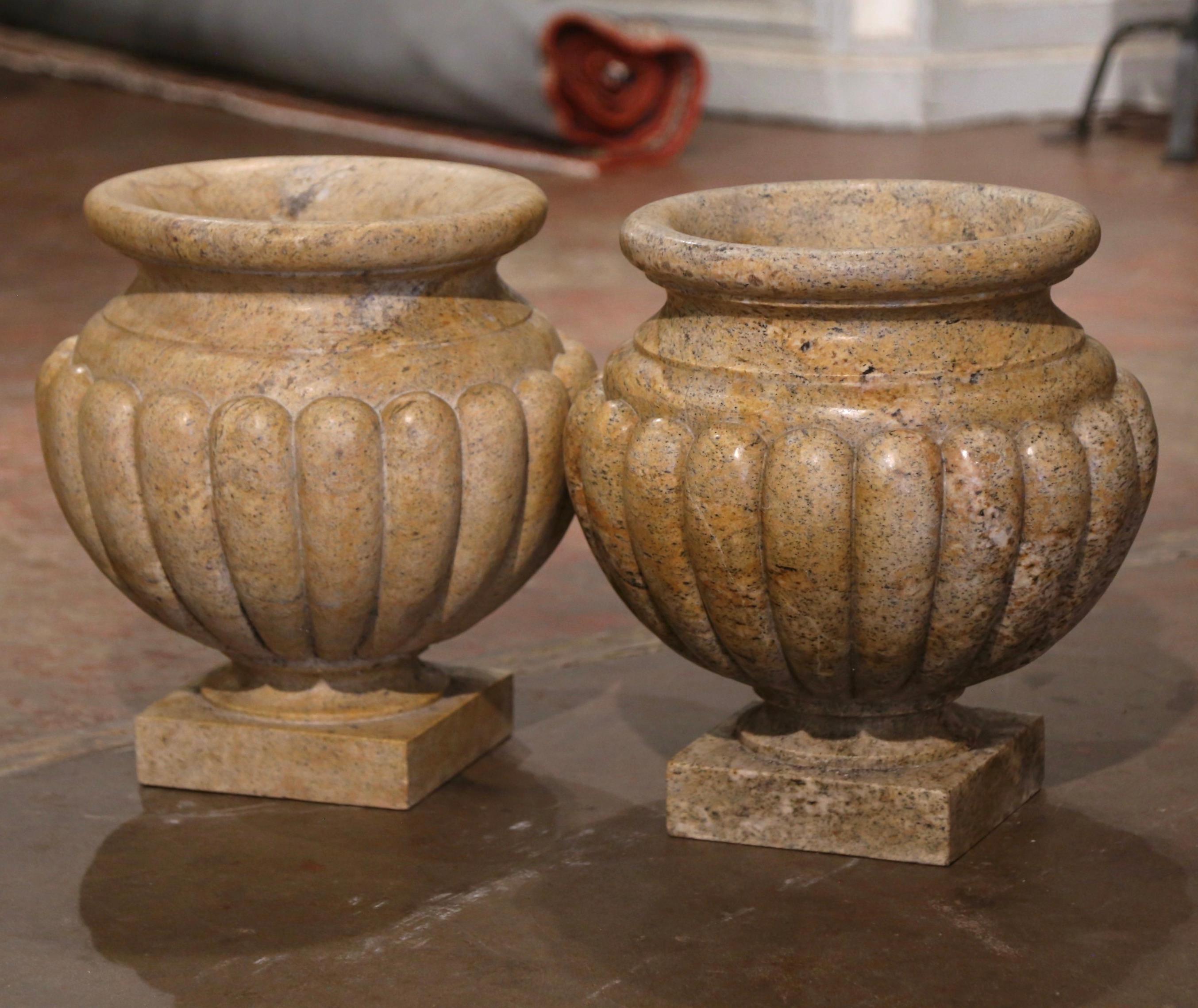 Crafted in Italy circa 1950 in the neoclassical style and made of hand carved granite, the antique planters have a stately, elegant style. Each vase stands on a square base over a fluted and gadrooned body with flared rim with egg-dart molding. Both