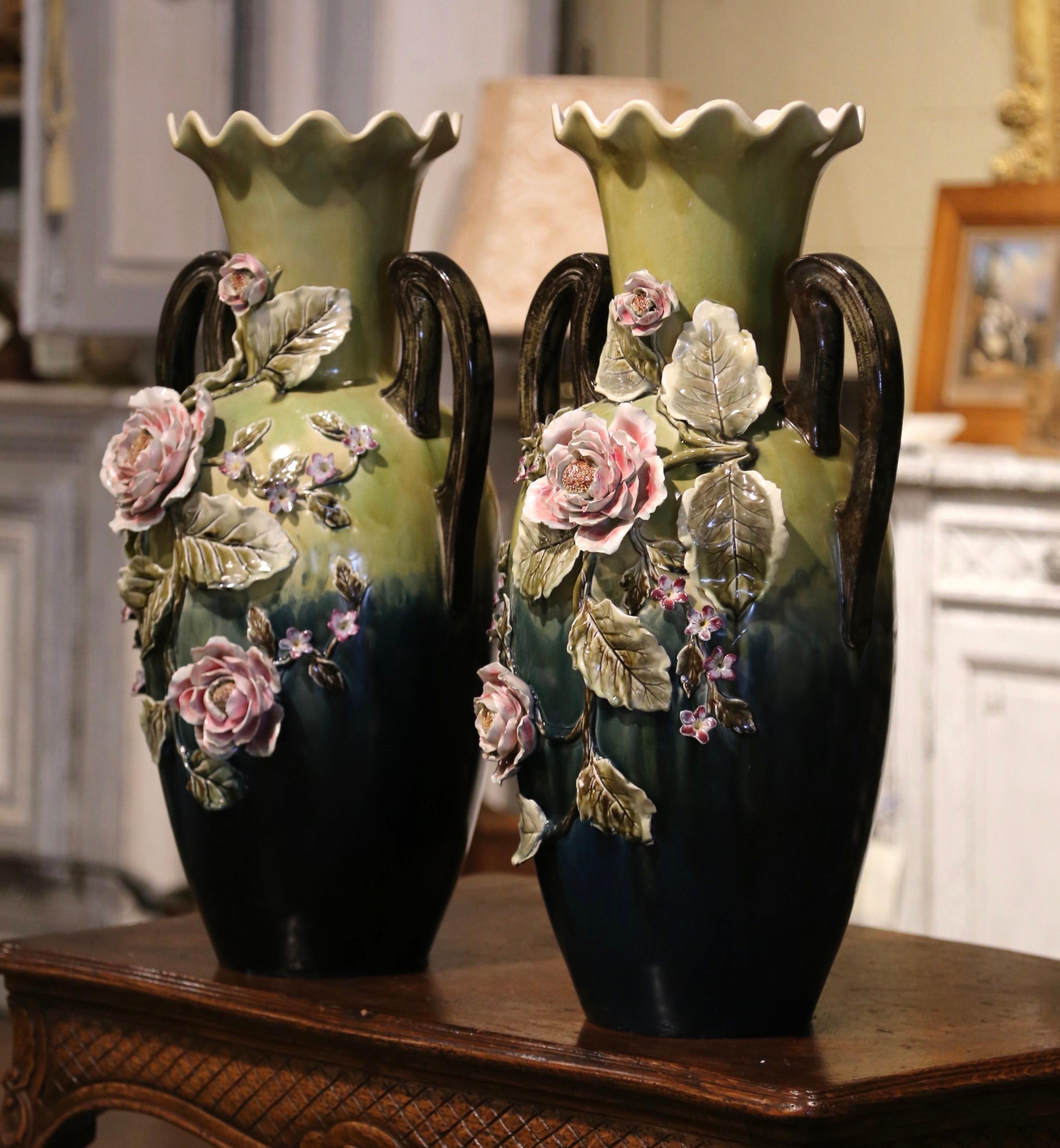 Magnifiquement sculptée et colorée, cette paire de grands vases anciens en majolique serait un merveilleux ajout à une cheminée, une table ou une étagère. Fabriqué en France, vers 1950, chaque pièce peinte à la main présente deux poignées élégamment