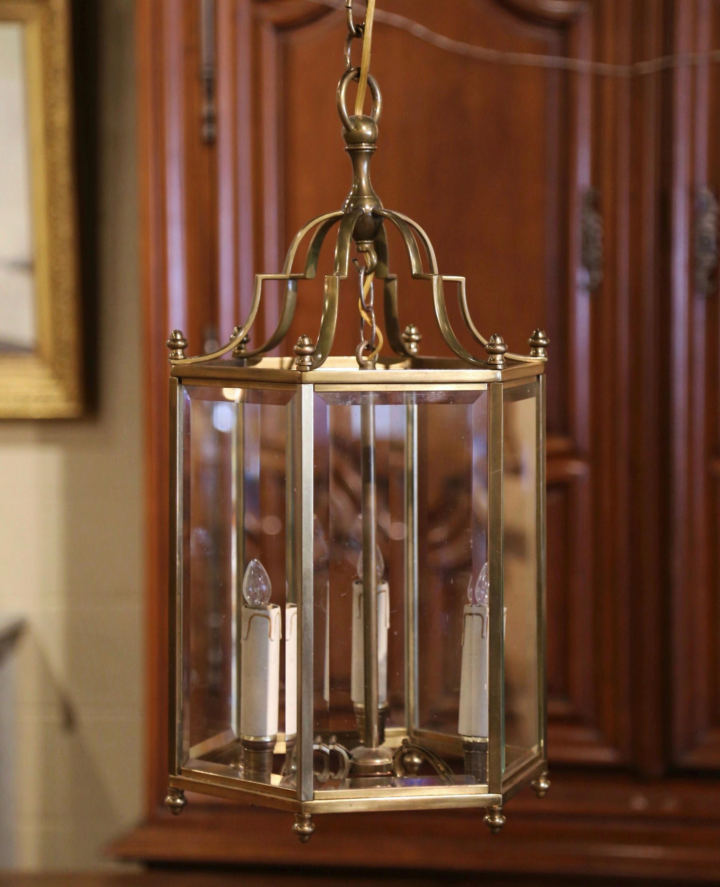 Illuminate your hallway with this pair of of brass lantern fixtures. Crafted in France circa 1960, each light
 with small round feet at the base is polygon in shape dressed with beveled glass and embellished with top finials; each fixture has three