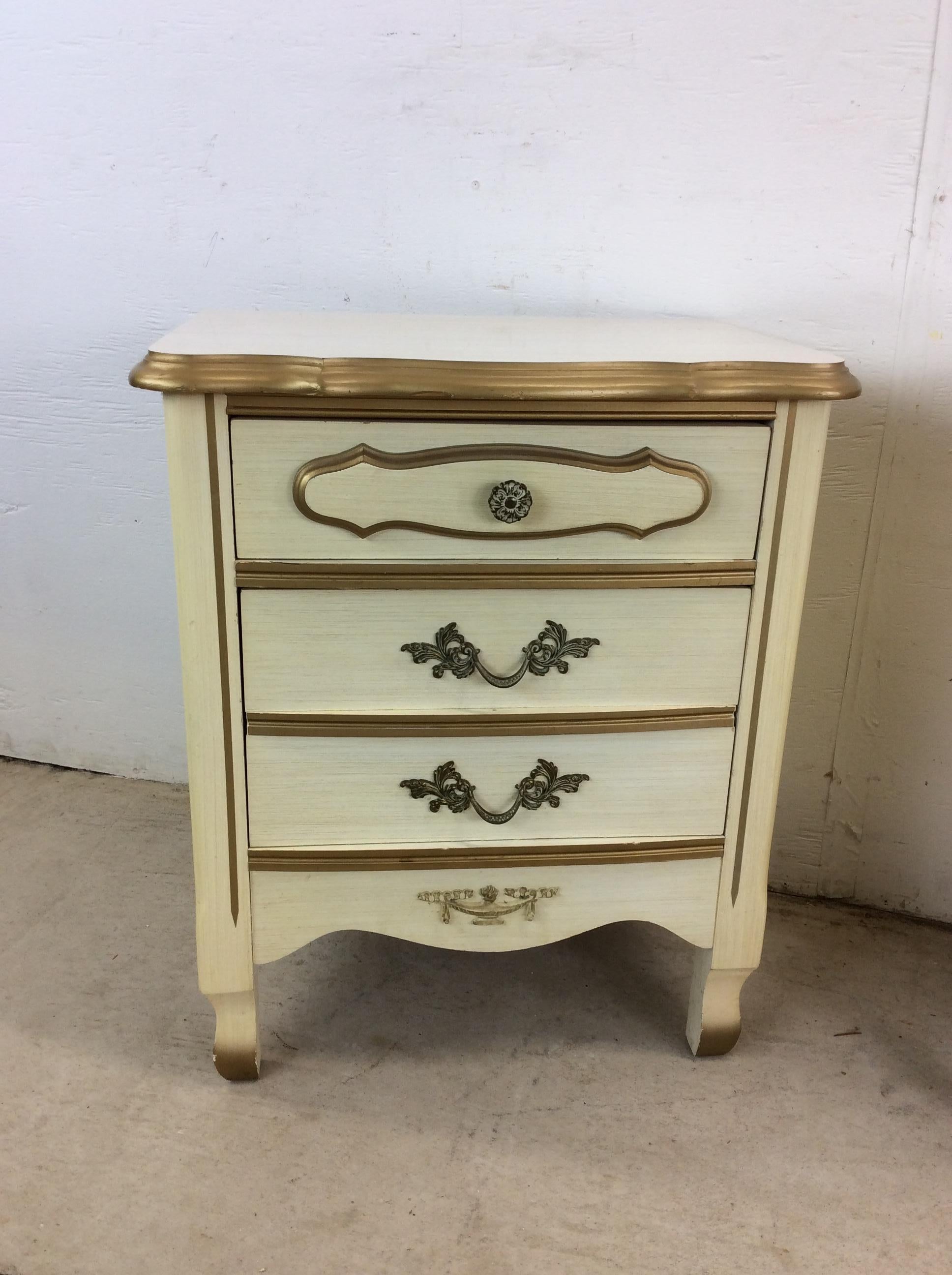 This pair of mid century French provincial style nightstands feature pressed wood construction, white lacquer finish with gold painted trim, two dovetail drawers with ornate hardware and tall tapered legs.   These nightstand are not a perfect match.