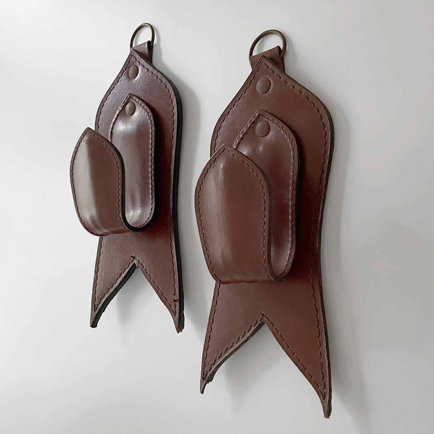 Pair of Mid Century French Saddle Leather Wall Coat Hooks in the style of Adnet 
France, mid century 
Gracefully sculpted, rich saddle leather panels with dovetail detailing  
Minor loss around the edges
Wall mounted single hook with hoop that