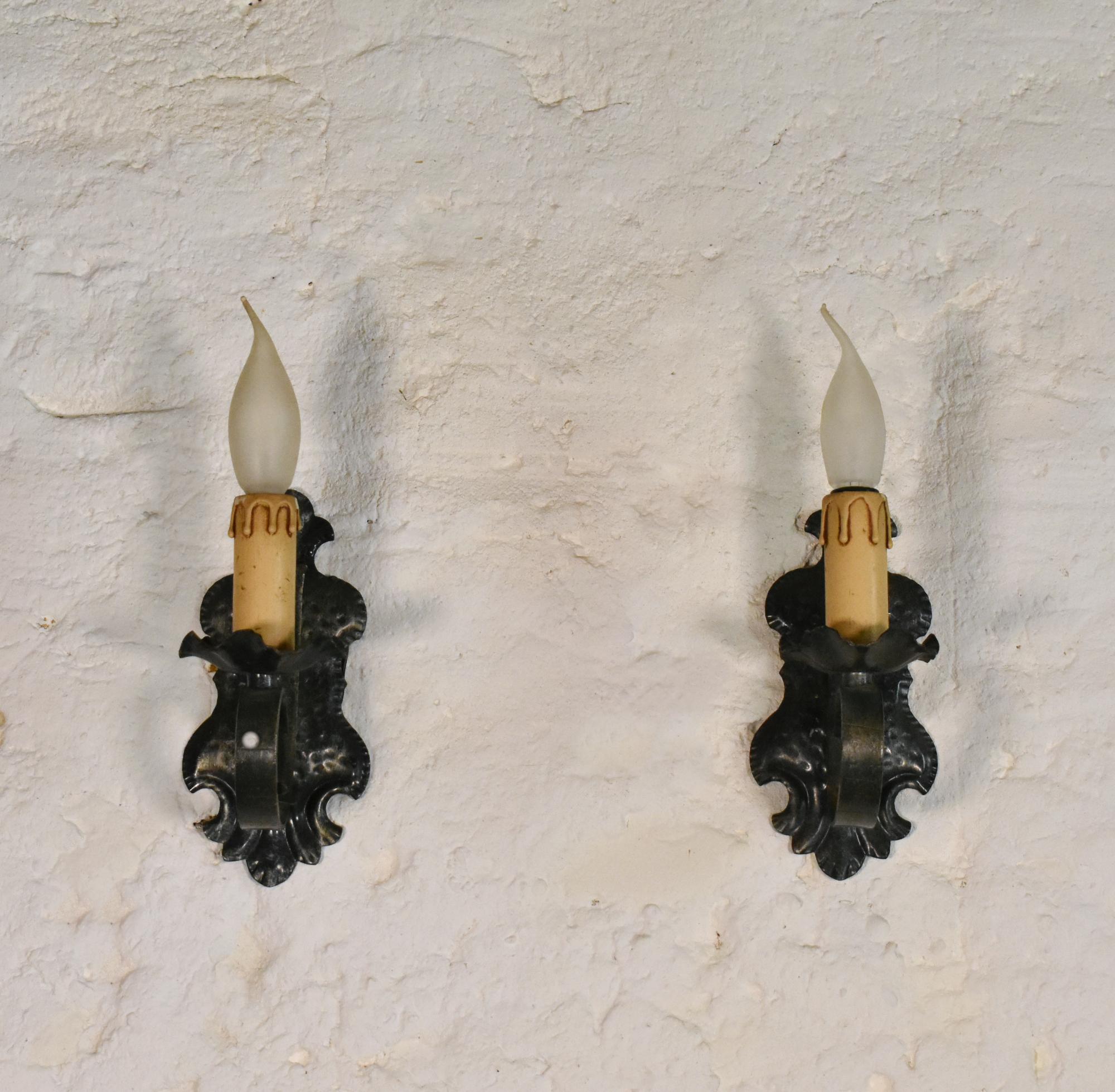 Pair of Mid Century Gothic Tole Wall Sconces
 
A pair of matching Gothic Tole Wall Sconces mounted on a pressed metal backdrop featuring floral decoration and lit by screw-in candle light bulbs.
 
The well-aged blackened patina adds to the character