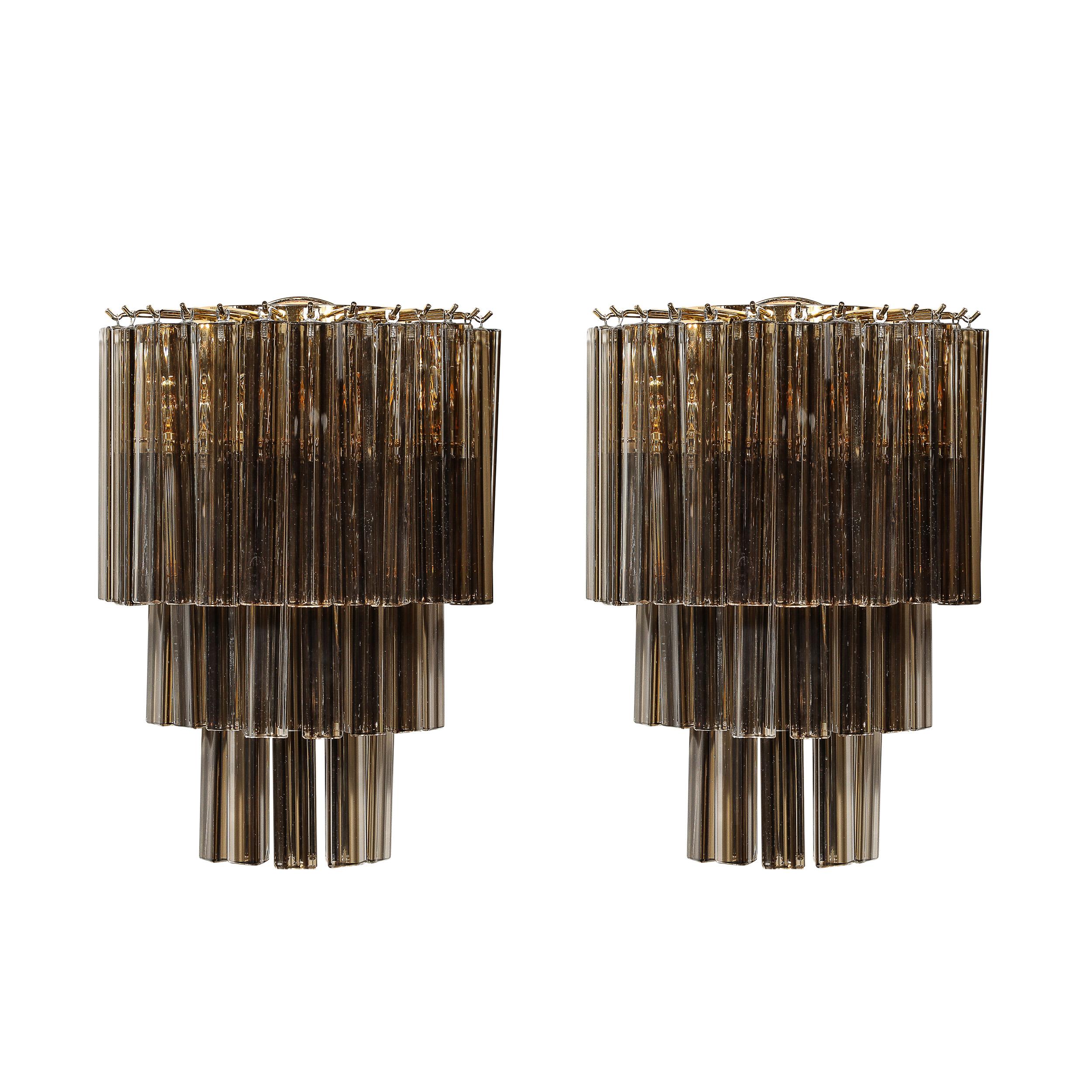 This gleaming and elegant Pair of Mid-Century Modernist Hand-Blown Murano Glass Three-Tier Triedre Sconces In Smoked Bronze W/ Brass Fittings originate from Italy, Circa 1970. They feature a tiered composition of hand-blown smoked bronze murano