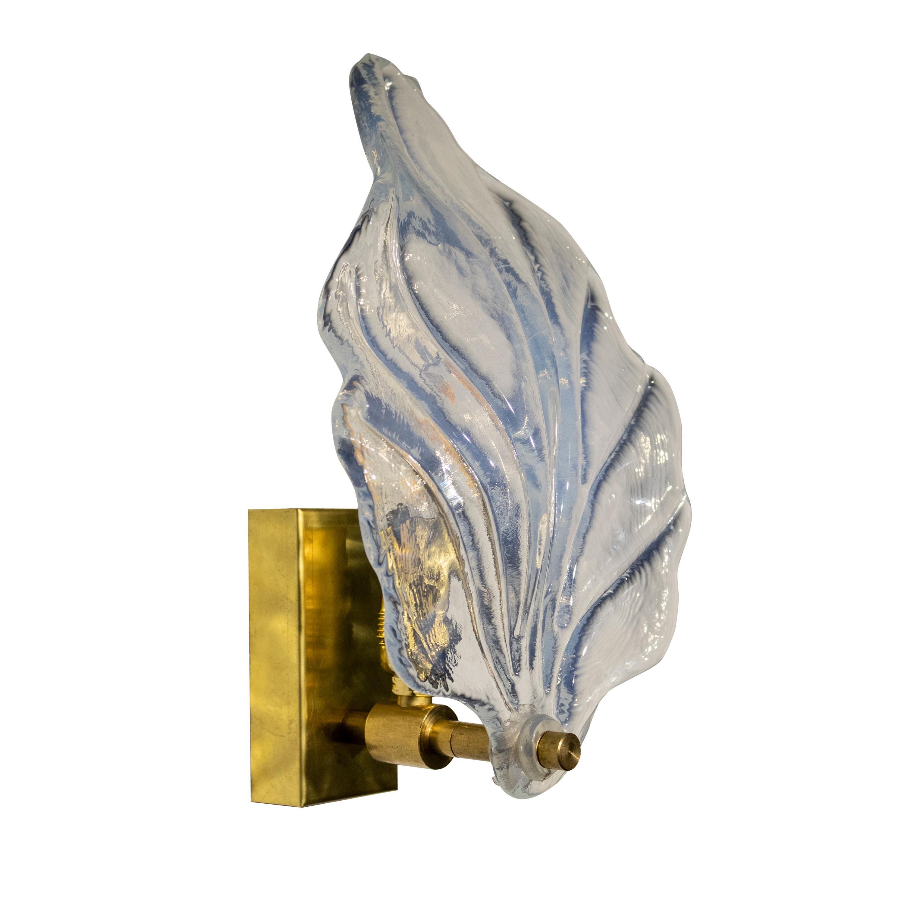 A pair of sculptural Murano glass sconces. Each lamp consists of a leaf- shape glass with a rectangular brass structure.
The sconces are made of hand-carved and hand-molded transparent Murano glass with veins and lines