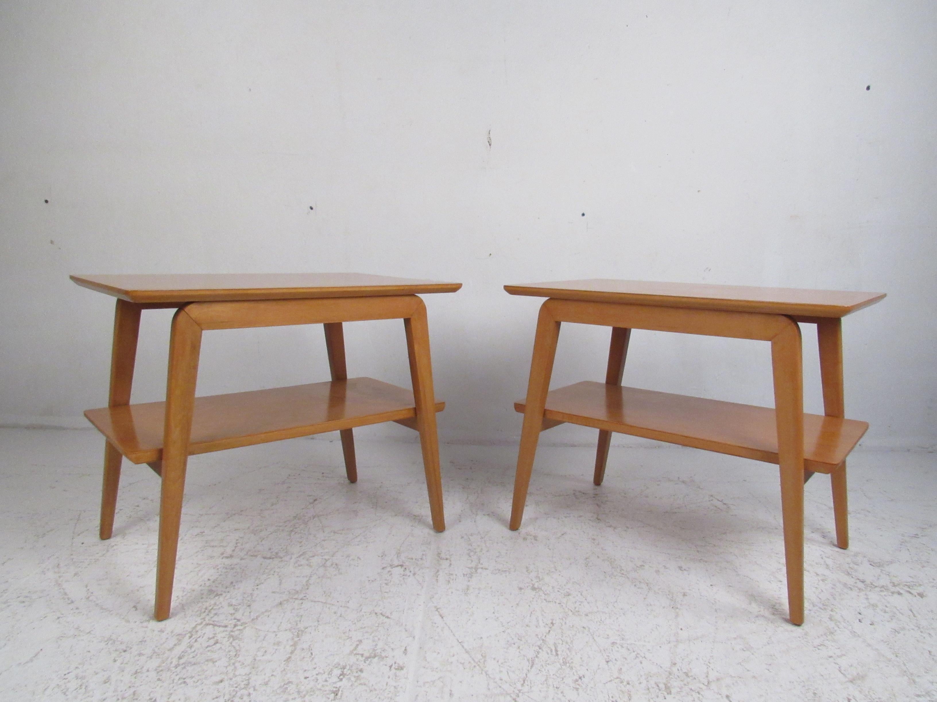 This beautiful pair of Mid-Century Modern two-tier side tables boast angled legs that taper downward and a vintage maple finish. The sleek design with a lower shelf ensures plenty of room to set and store items. This stylish pair of end tables make