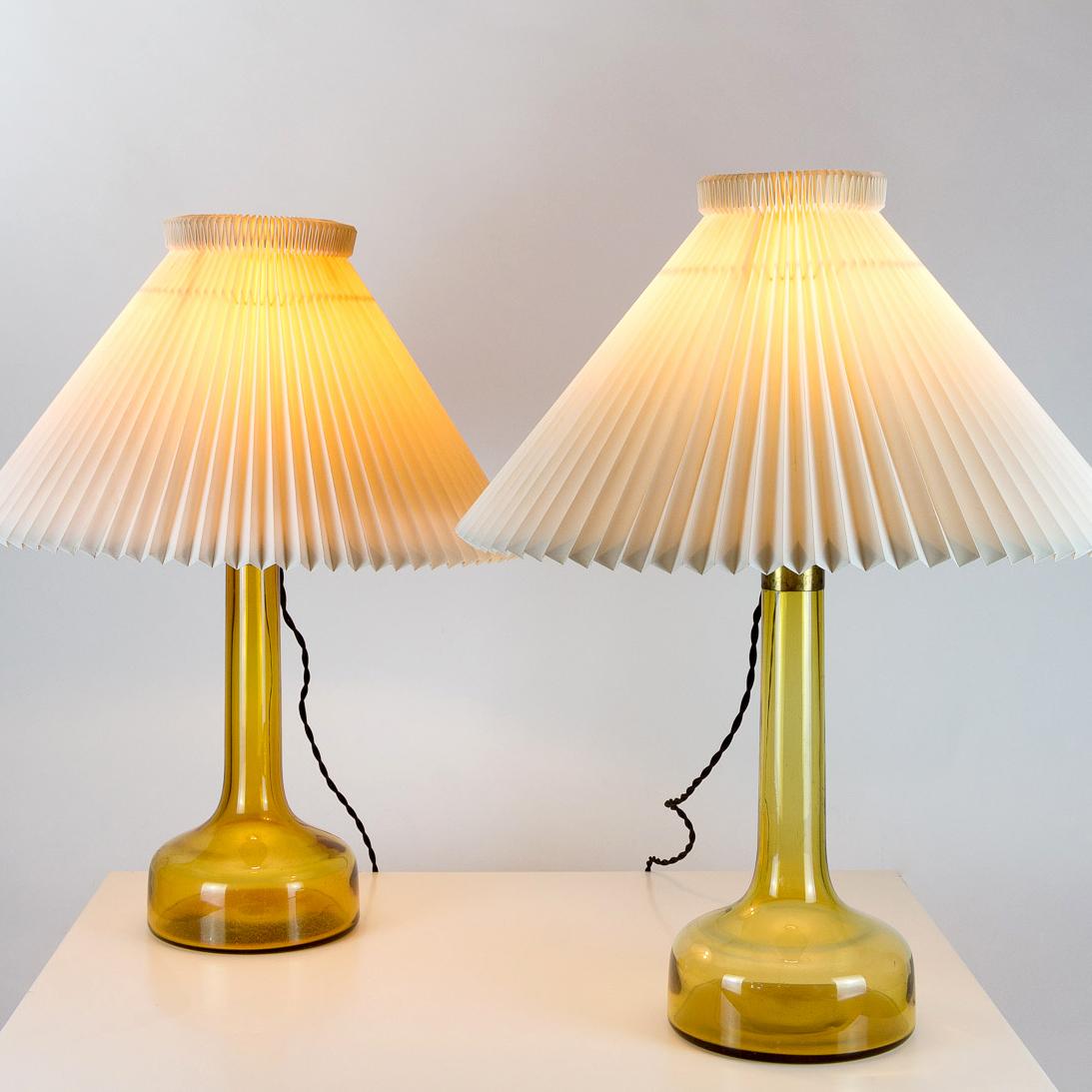A near pair of midcentury yellow glass table lamps by Holmegaard for Le Klint with original Le Klint Shades. Measures: Base diameter is 19cm, shade diameter is 50cm, approximately 10cm difference in height due to different brass bulb holders. Some