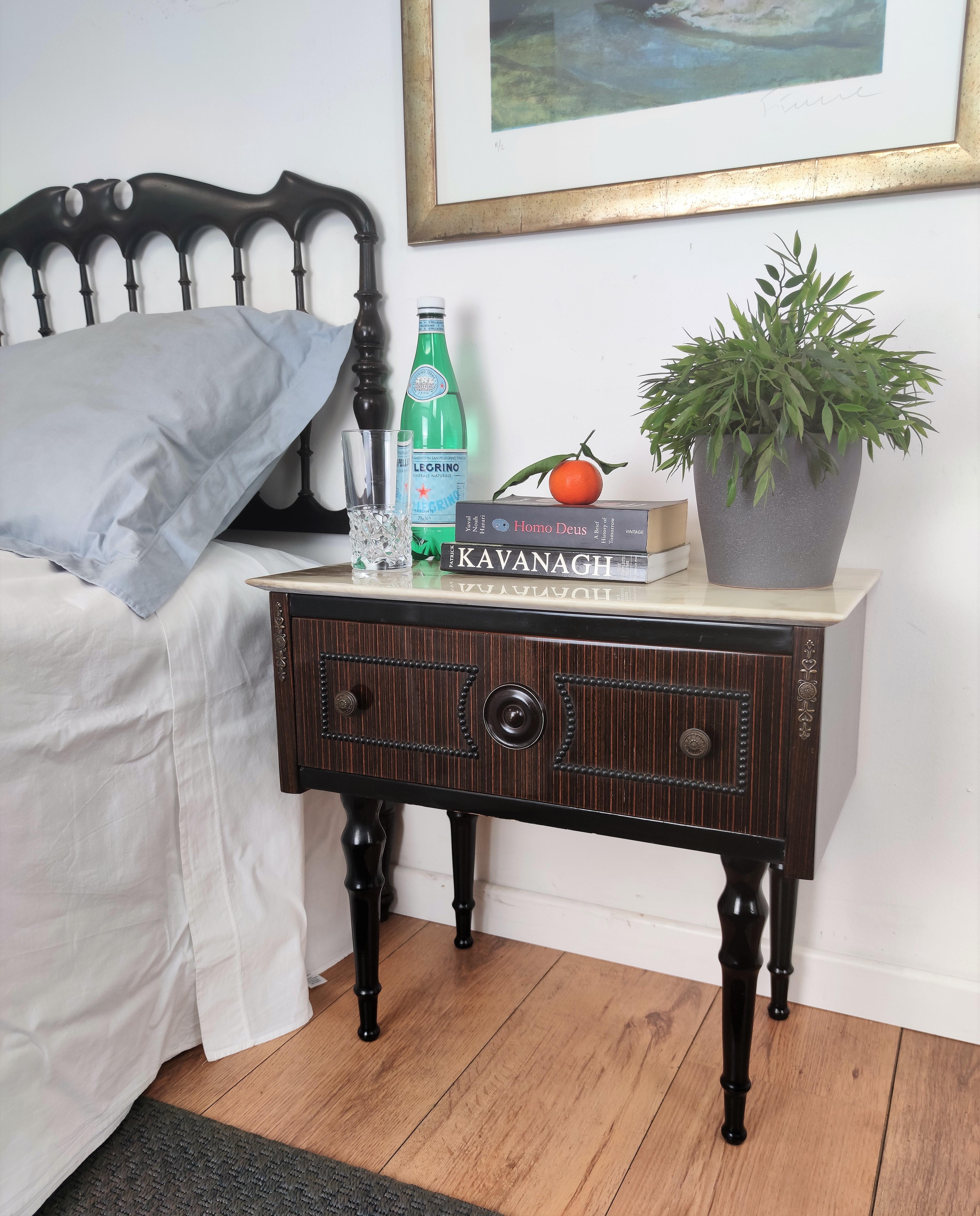 Very elegant and refined Italian 1950s Mid-Century Modern, neoclassical, in typical Art Deco design, pair of bedside tables with front drawer, white marble top and brass details such as the 2 handles and the carved legs. 

Those pieces, in the