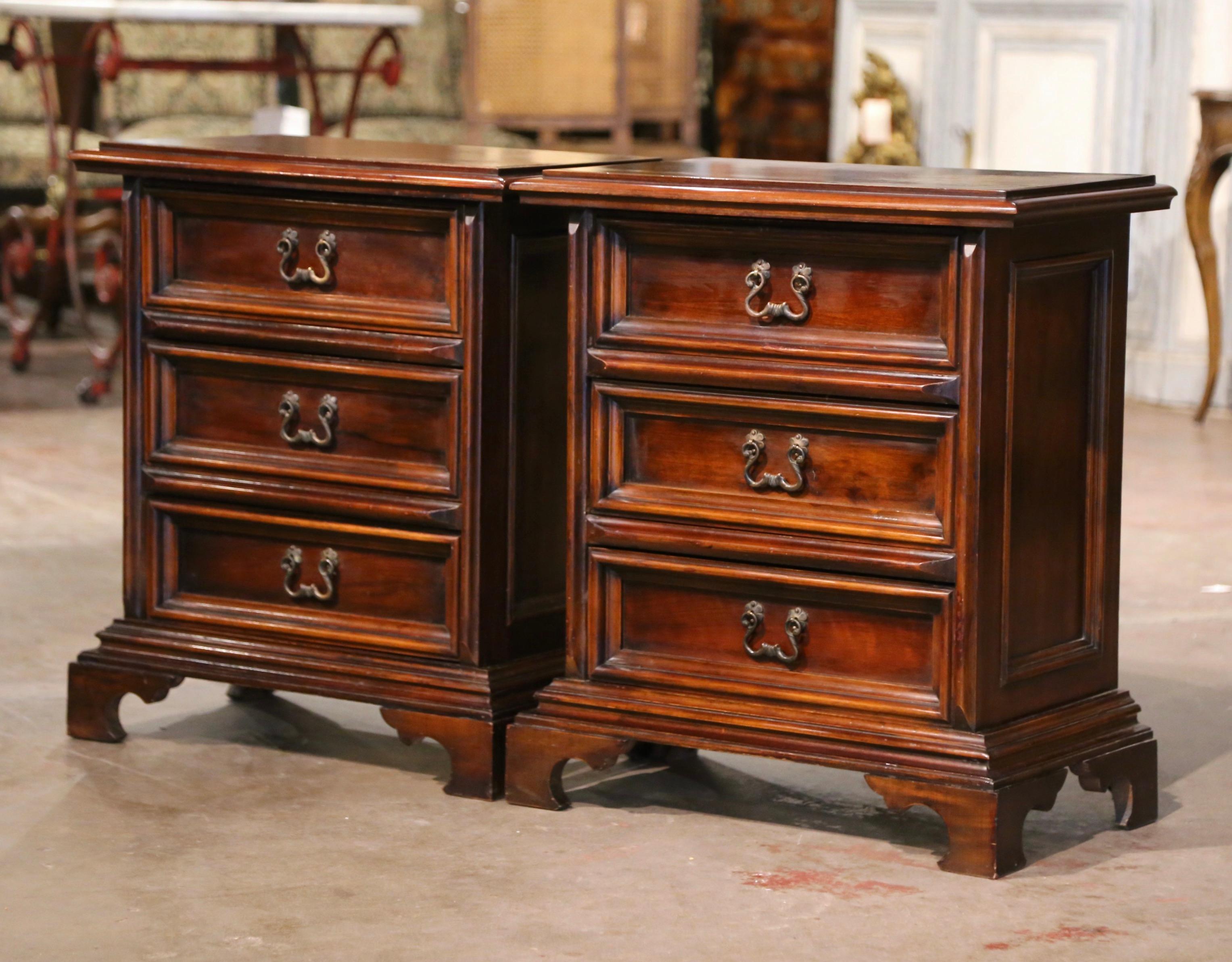 Decorate a master bedroom with this elegant pair of antique nightstands. Crafted in Italy circa 1970, each chest stands on bracket feet over a thick straight plinth; the cabinet features three recessed paneled drawers decorated with brass pulls. The
