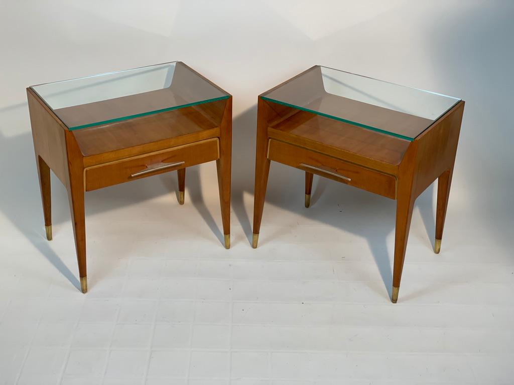 1950's Italian bedside tables with four tapered legs ending in brass, cherry wood structure with elegant shape with drawer and double top, upper shelf in ground glass.
 Stylish handles in cast brass. 
This tables are finished on the back side and