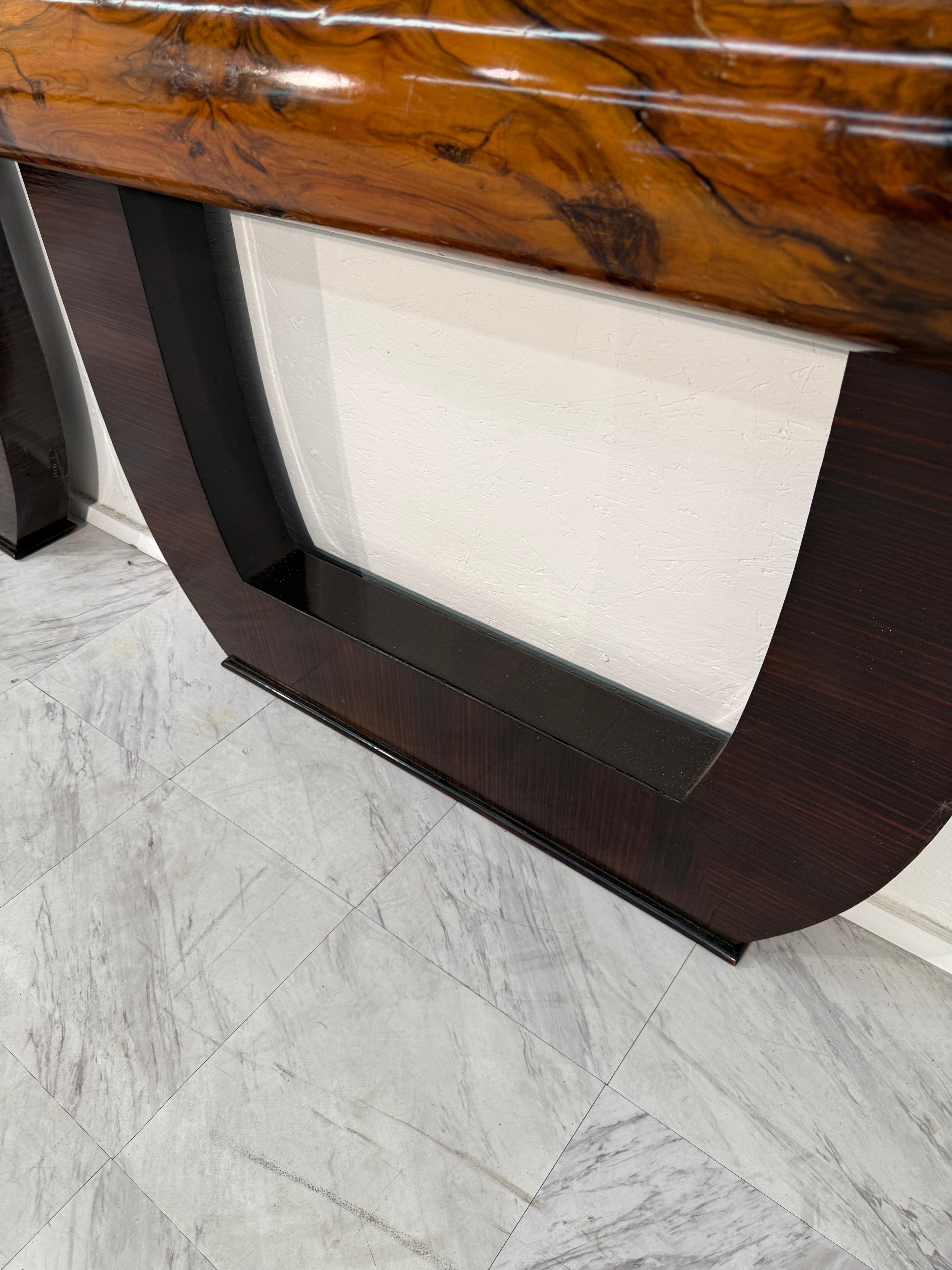 A sophisticated pair of Italian console tables from the mid-20th century, crafted with exceptional attention to detail. Each table features a sculptural U-shaped base in richly toned wood veneer, supporting a bold burl wood top with beautifully