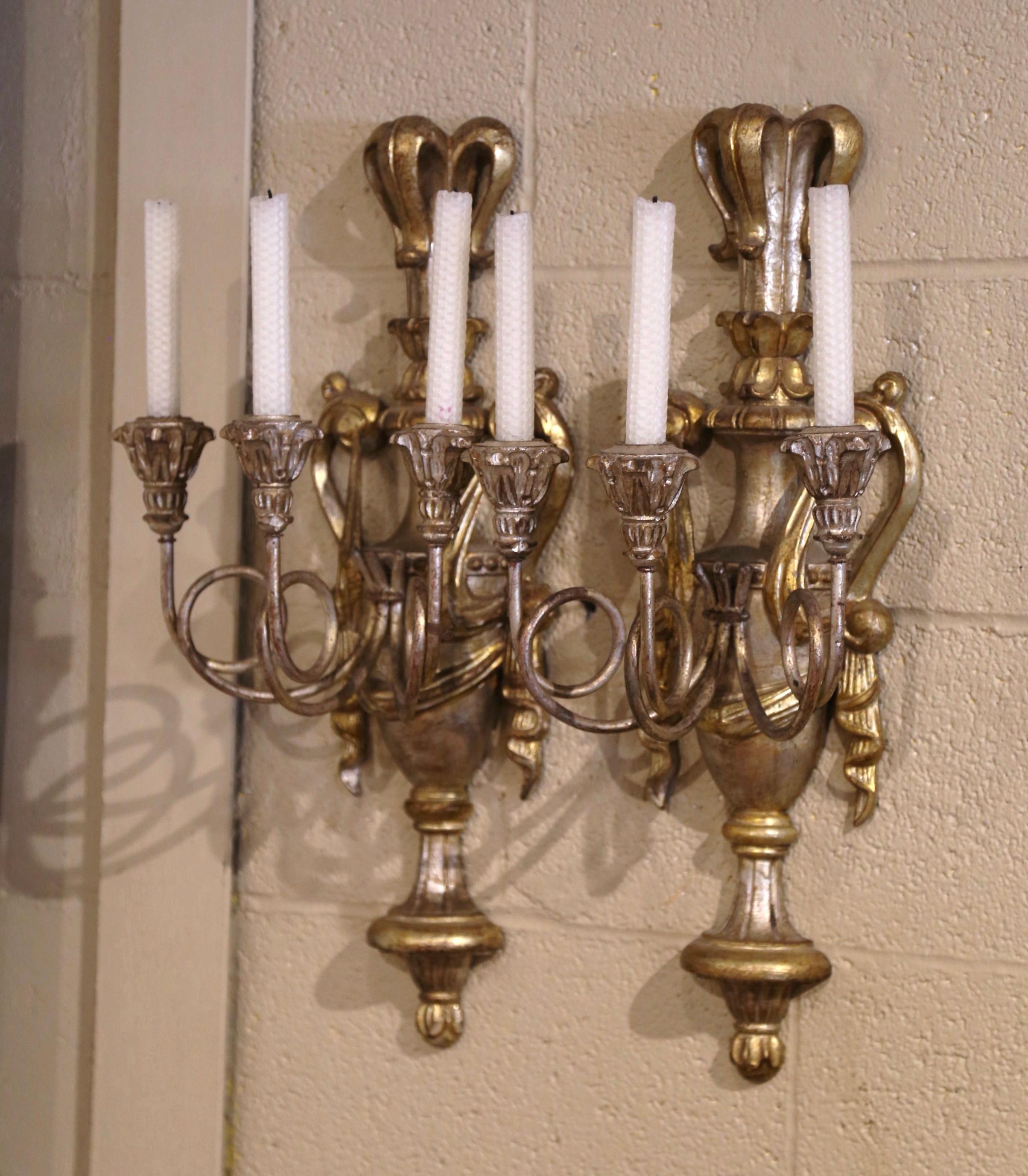 Make a dramatic, romantic statement in your home with this elegant pair of wall fixtures. Crafted in Italy circa 1970, each large sconce features a hand carved vase flanked with draped swags embellishments on either side; the pediment is further