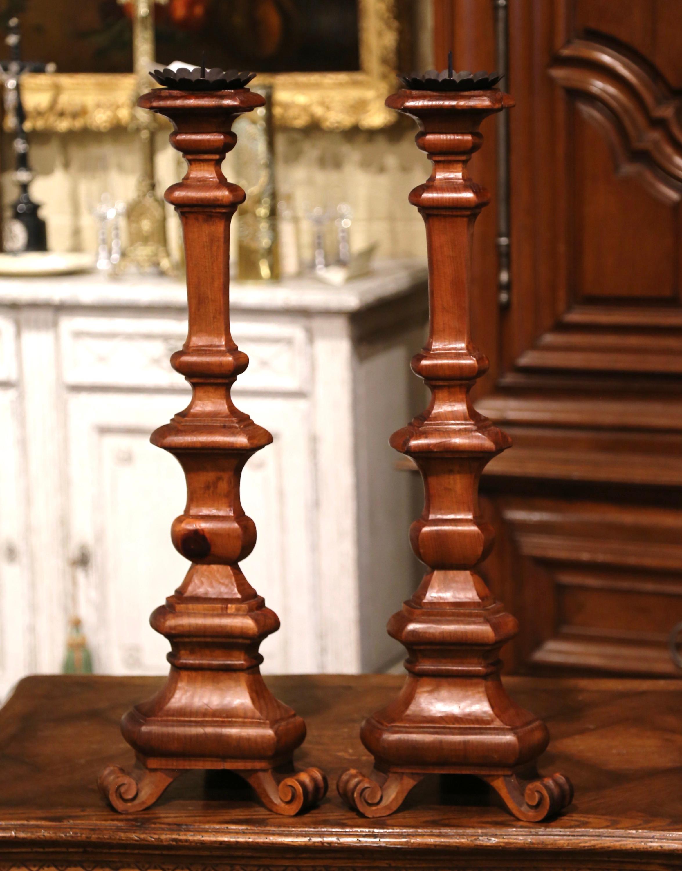 Decorate a console or buffet with this elegant pair of vintage candlesticks. Created in Italy circa 1960 and made of elm, each candle holder stands on three scrolled feet over a triangle base and a tall carved stem embellished with bobeche and